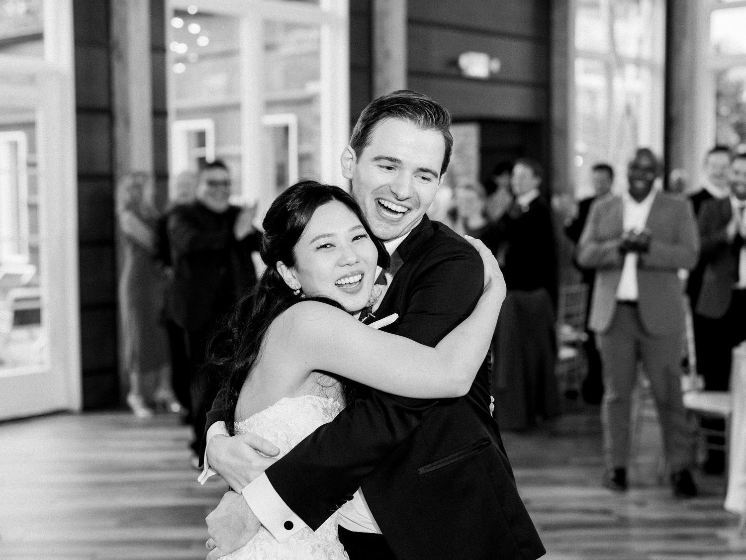 Black and white photo showing joyful dancing and celebration at an indoor wedding reception.