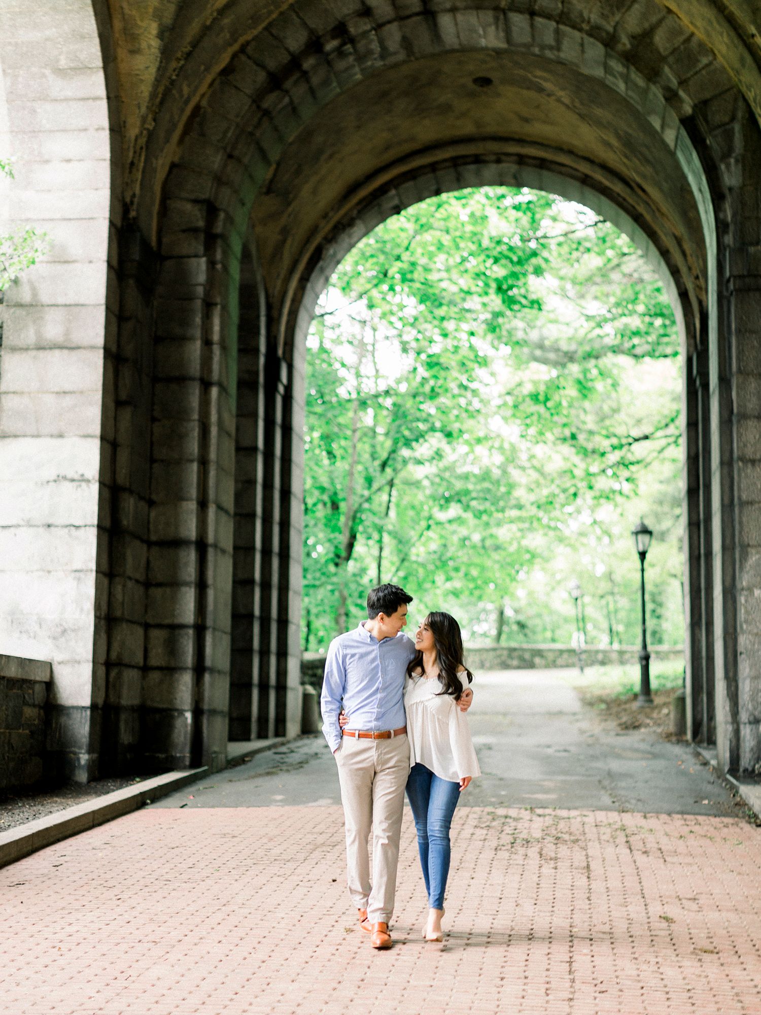 A couple walking through a historic stone archway surrounded by greenery.