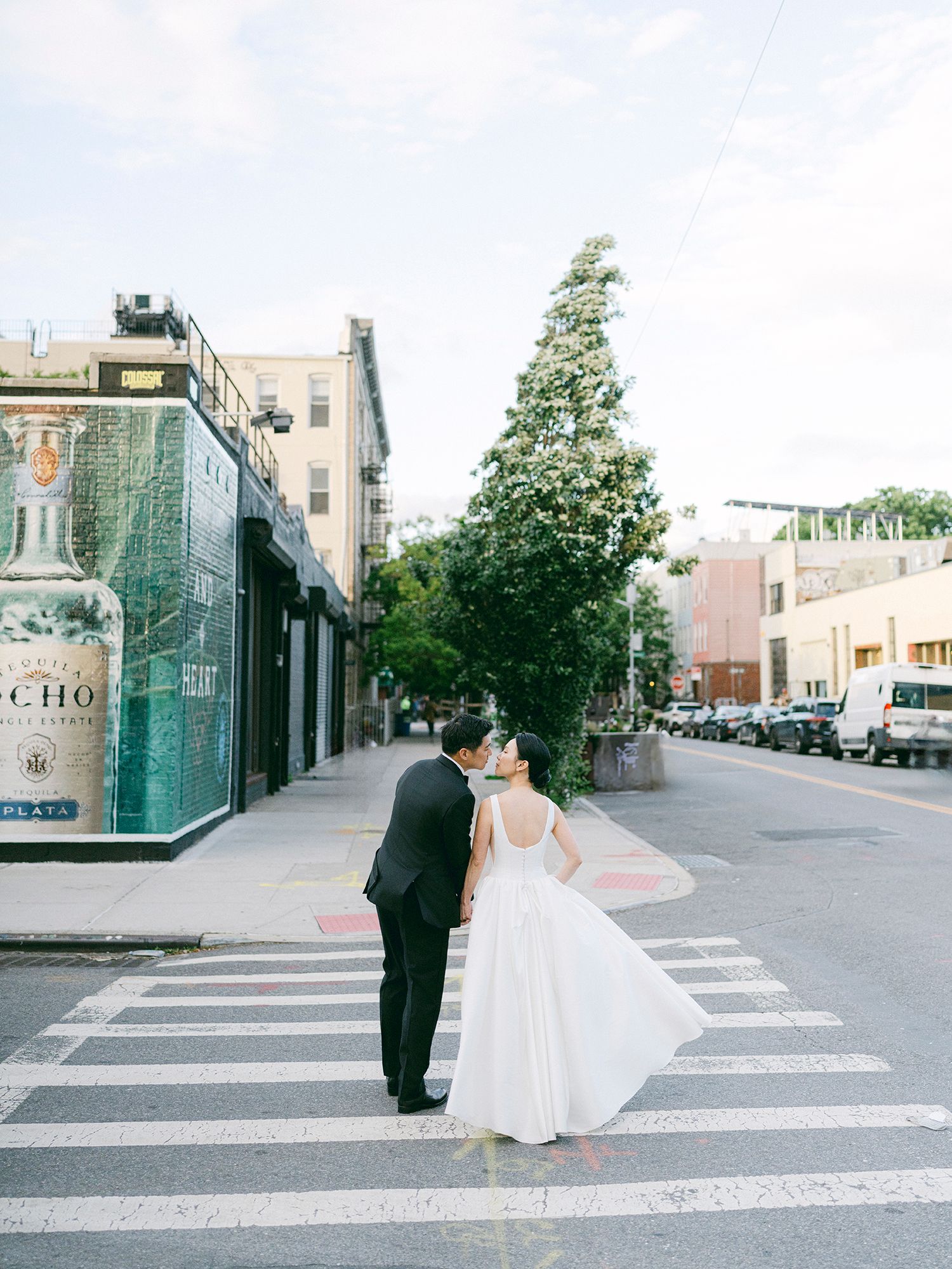 Couple in wedding attire walking across urban crosswalk on sunny day. NYC Wedding Photographer