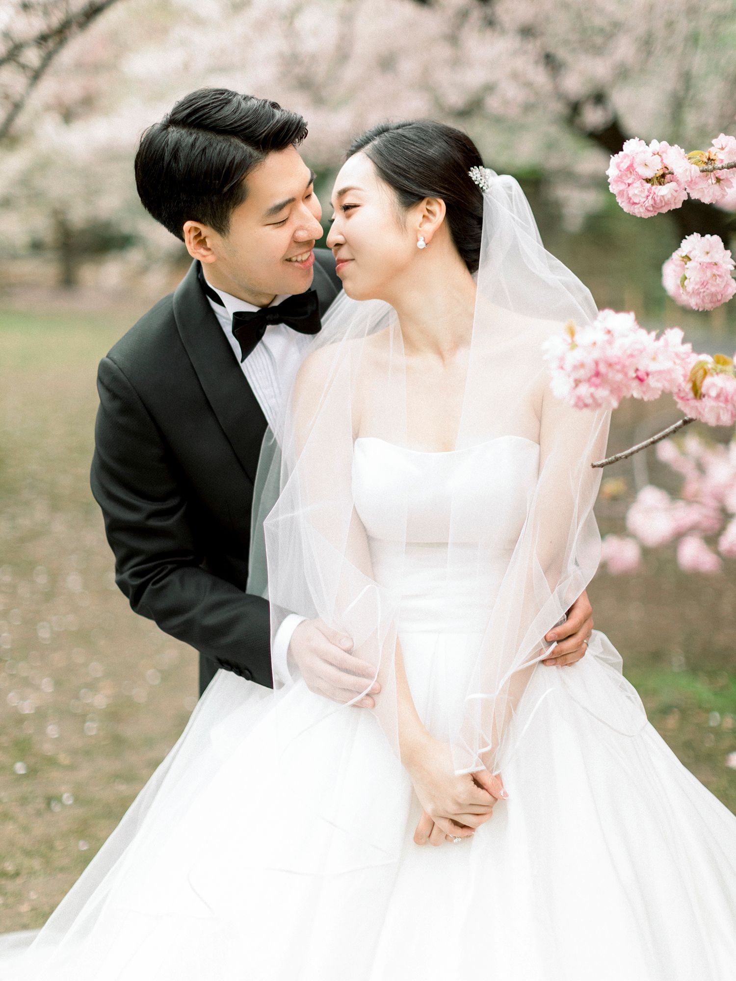 Intimate wedding portraits captured under cherry blossom trees with elegant white dress and veil. NYC wedding photographer.