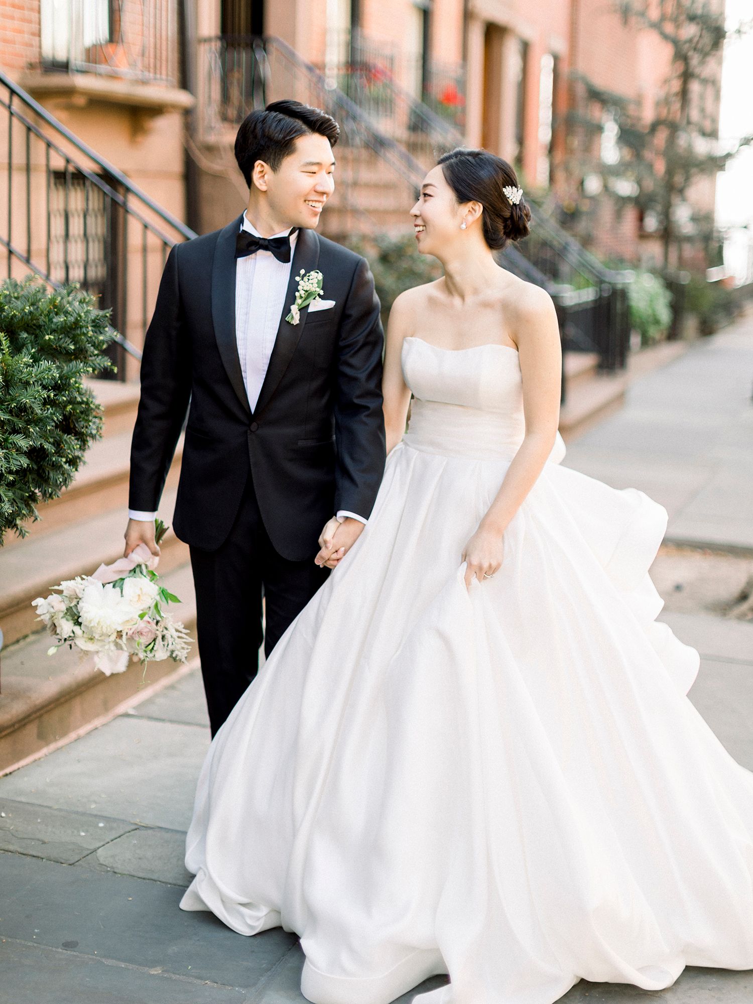 Elegant couple walking along a charming brick-lined street in formal wedding attire. NYC wedding photographer.