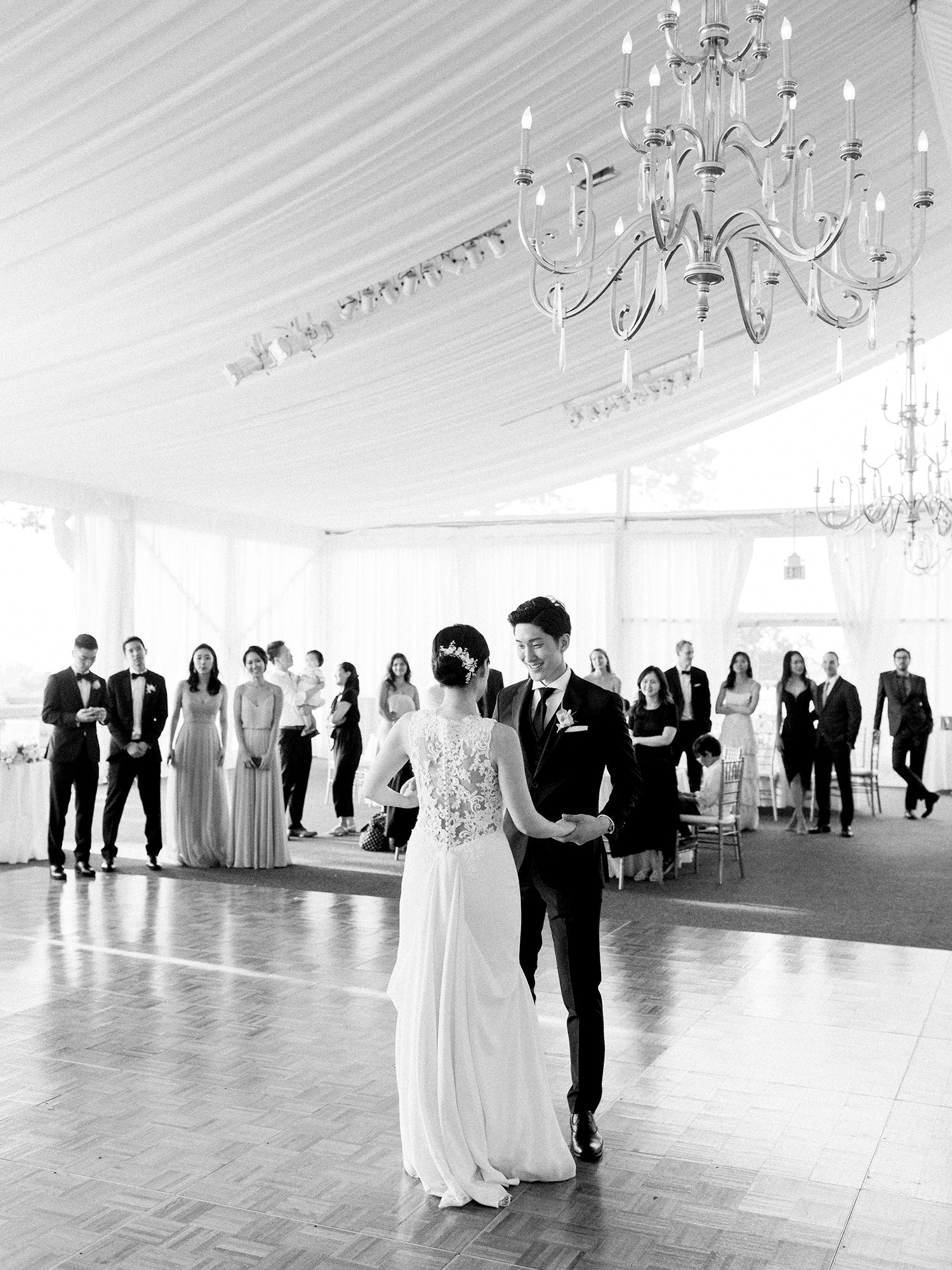 Wedding reception in an elegant white tent with crystal chandeliers and couples dancing.