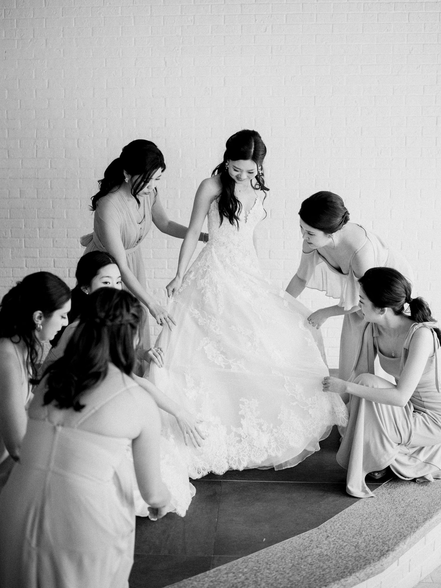 Black and white sequence showing bridesmaids helping adjust a wedding dress train on the floor.