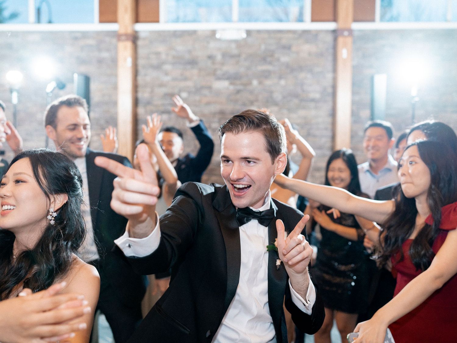 Wedding party celebrating with energetic dancing and laughter at an indoor venue.