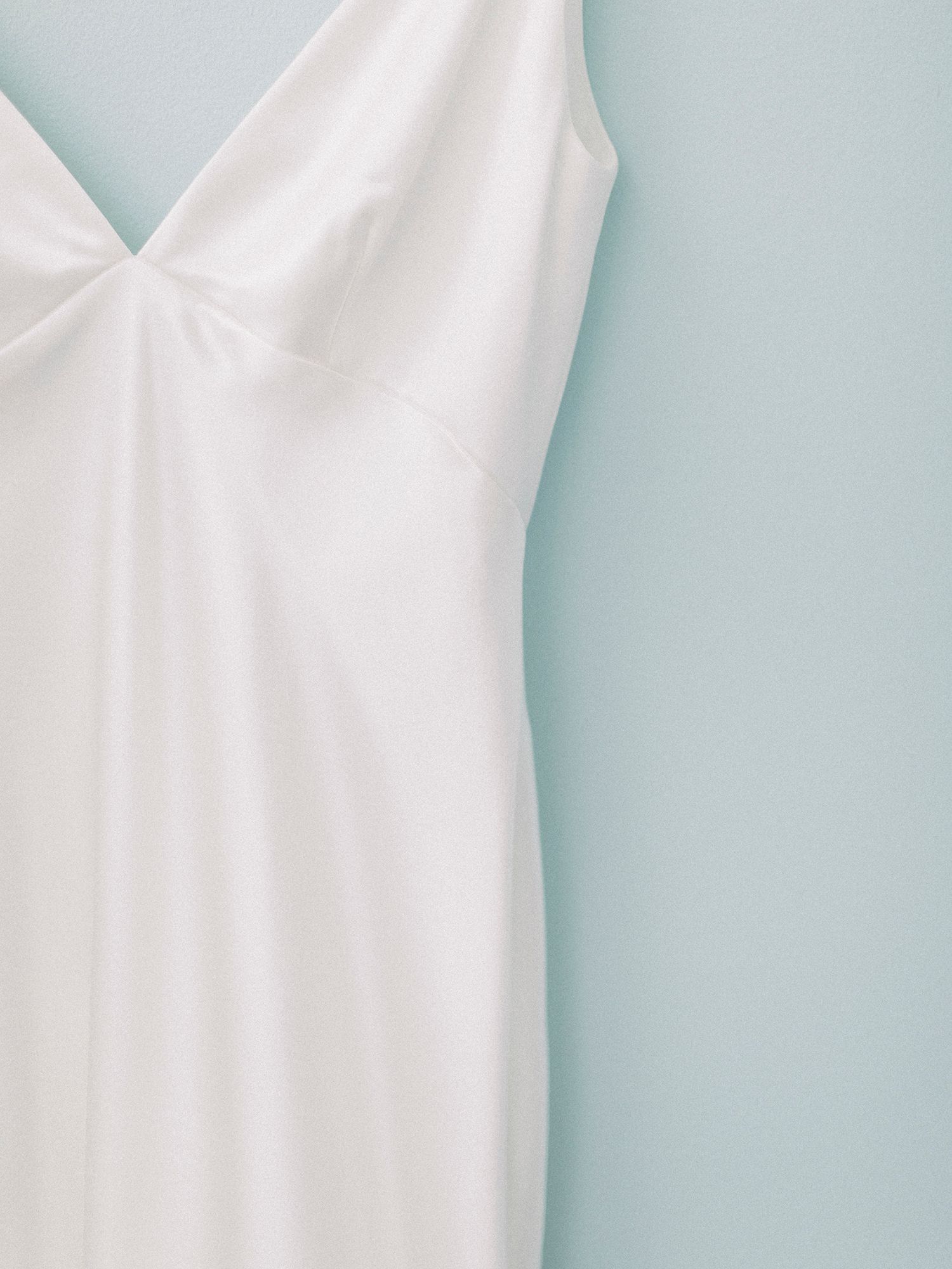 Elegant white wedding dress details hanging against a light blue wall.