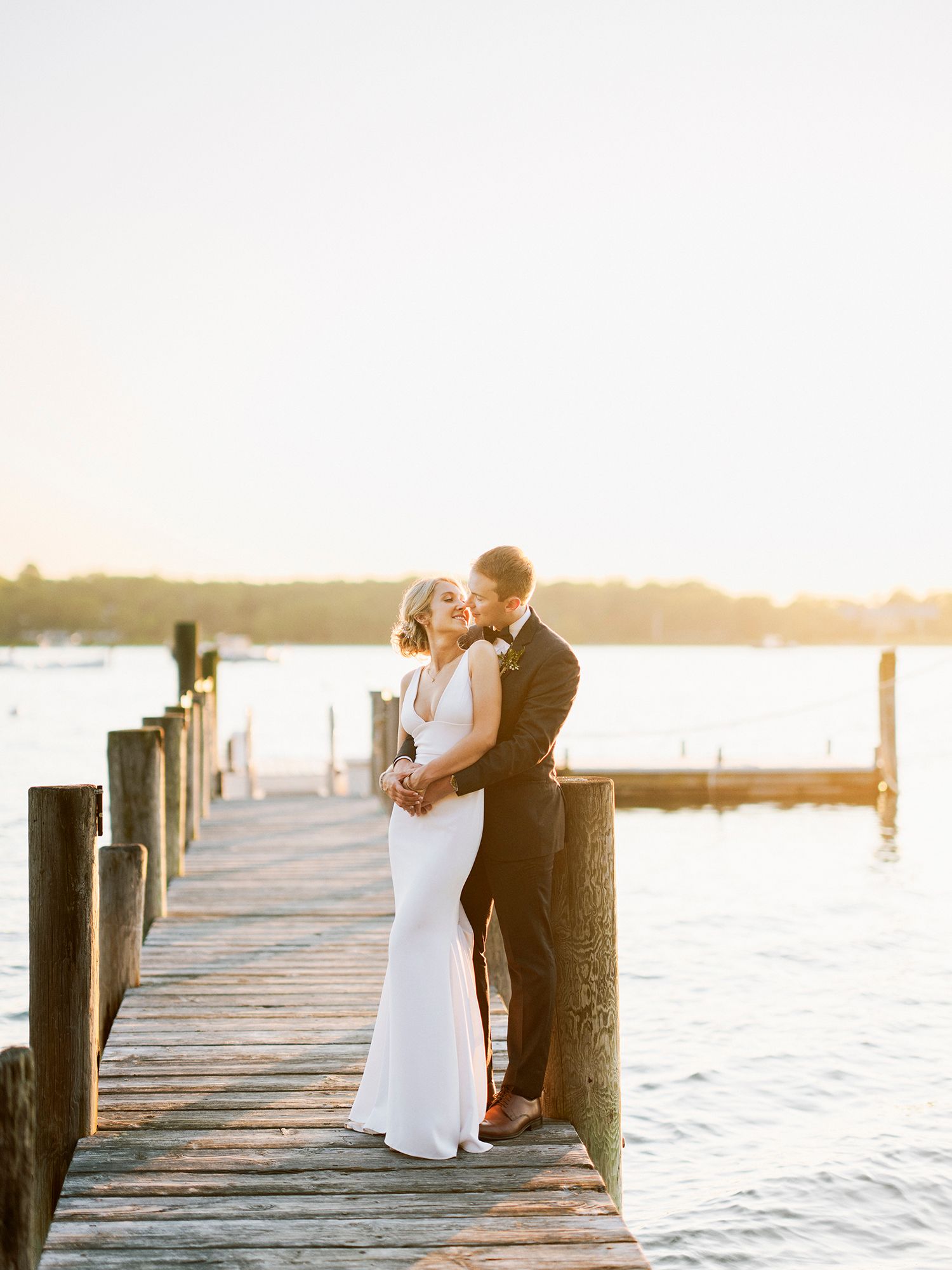 A romantic couple embraces on a wooden dock during golden hour with water views. NYC wedding photographer.