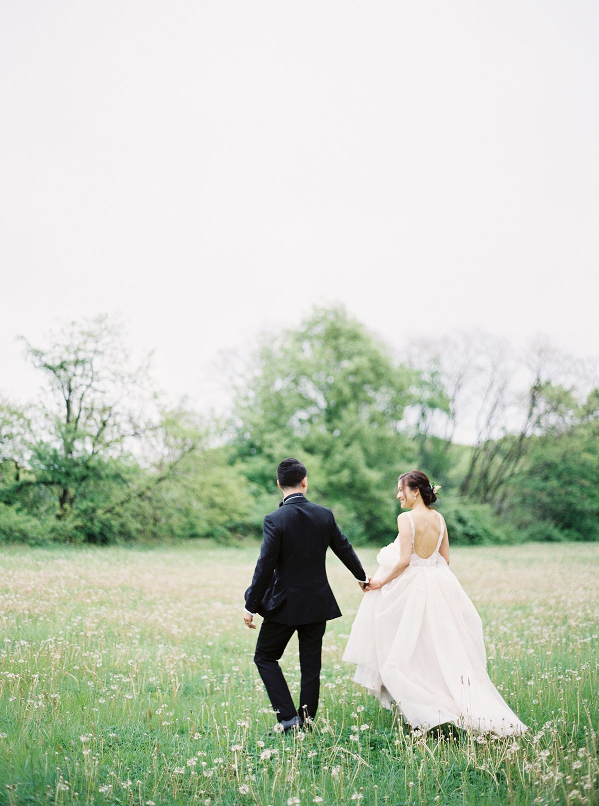 Couple runs through a wildflower meadow in wedding attire.