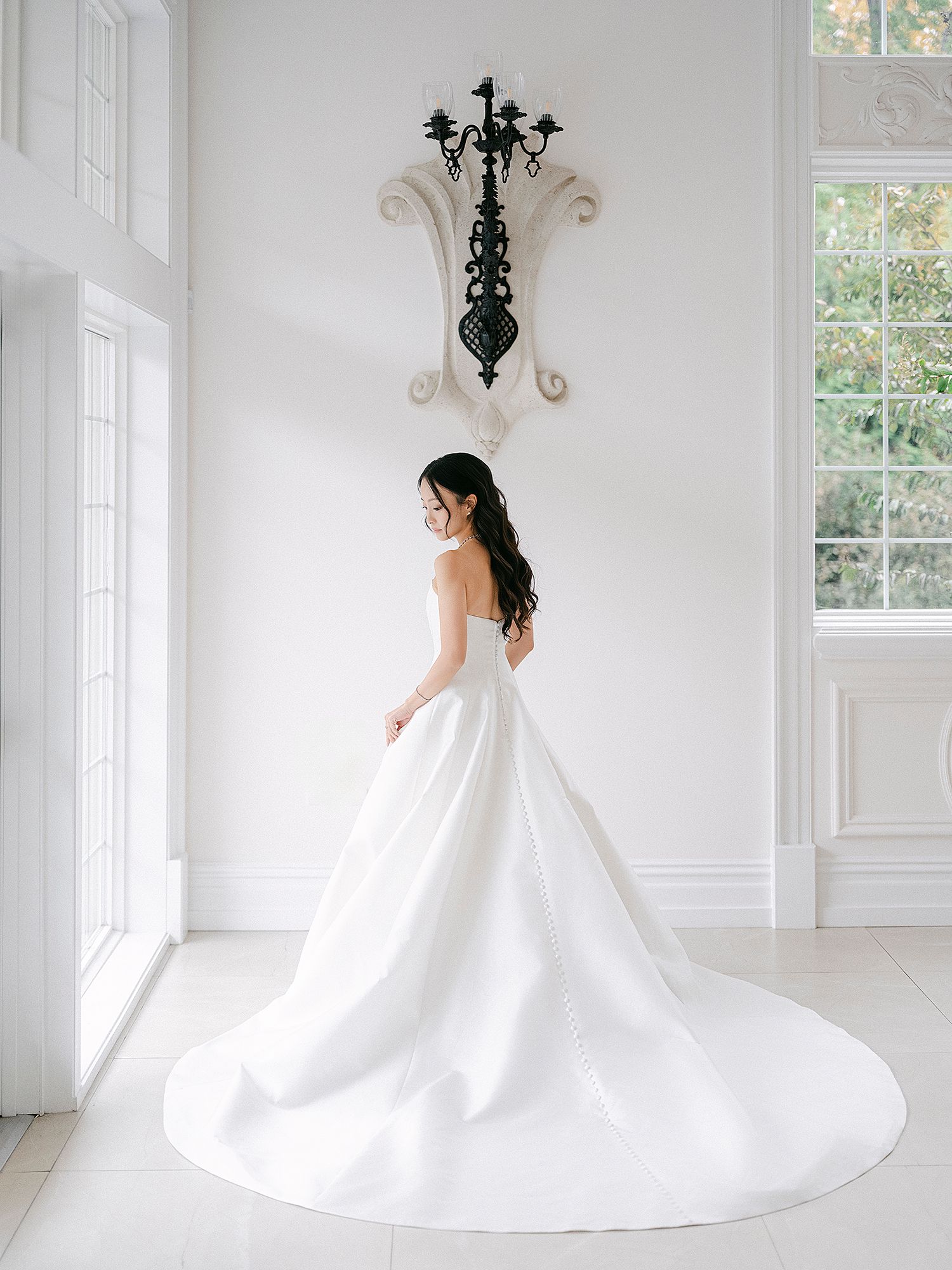 Elegant white wedding gown with flowing train in bright sunlit room with chandelier. NJ wedding photographer. Cly by Chung