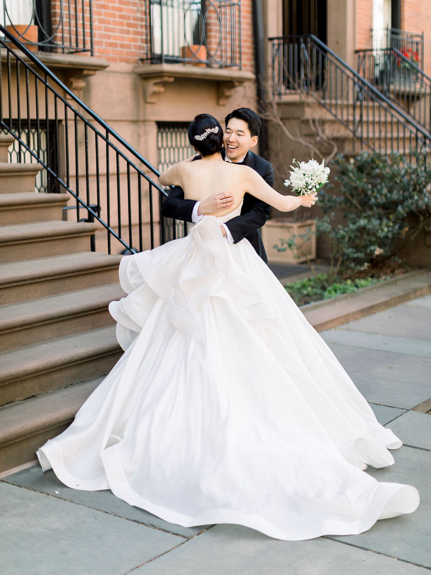 Bride in flowing white ballgown twirls gracefully on brownstone steps.