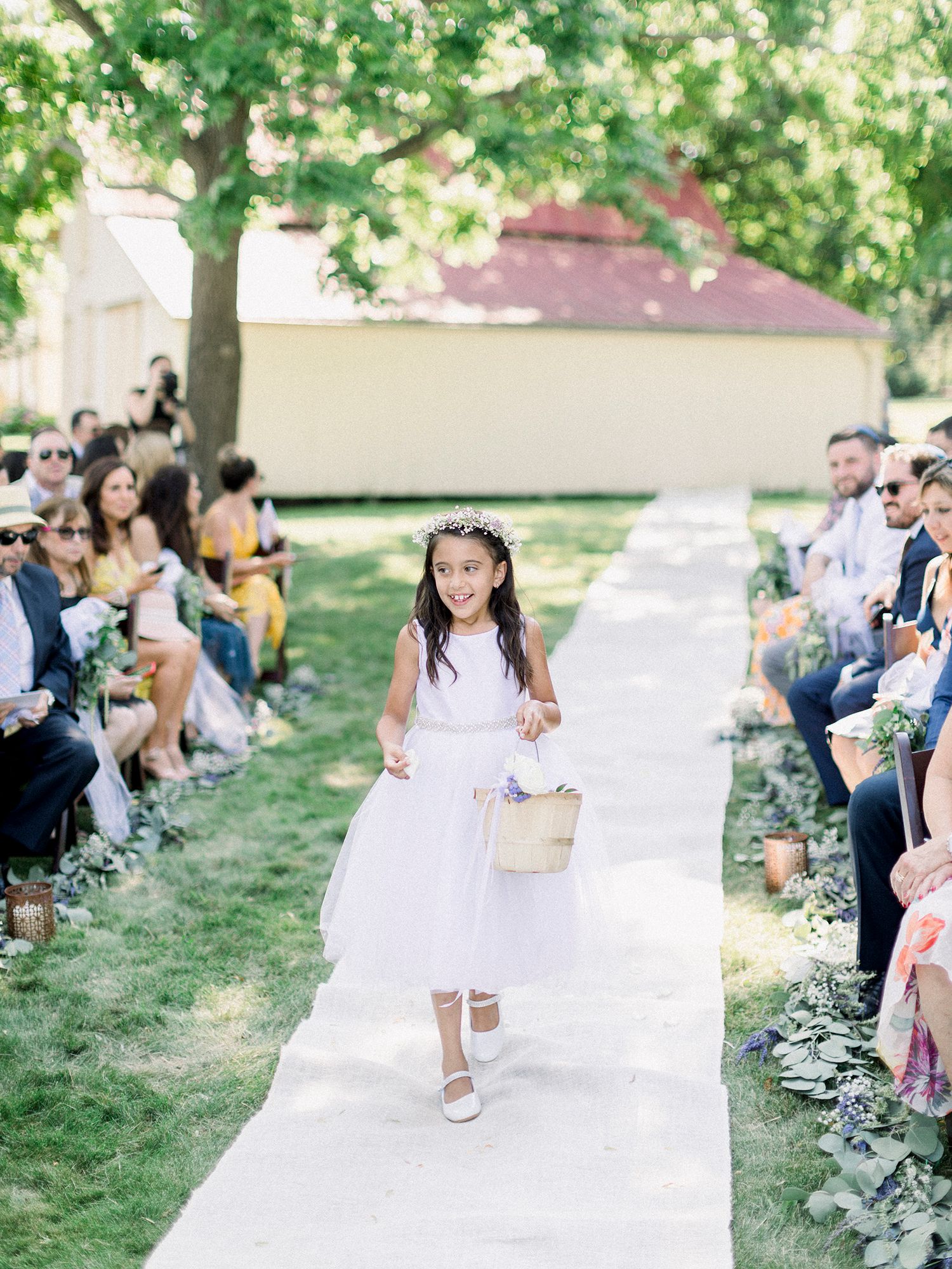 Wedding ceremony aisle runner stretches across green lawn under shady trees.