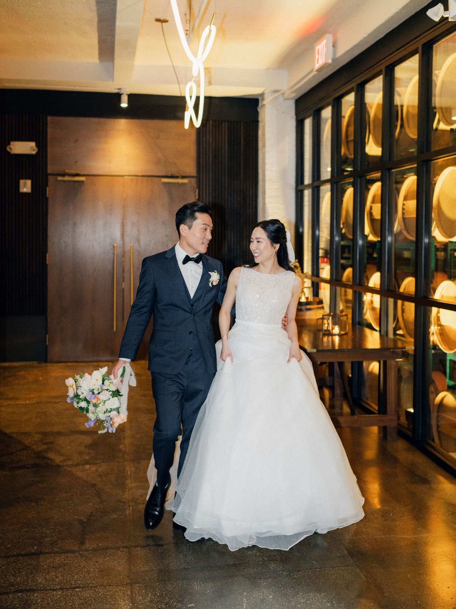 A couple in formal wedding attire walking through an elegant venue with illuminated display cases.
