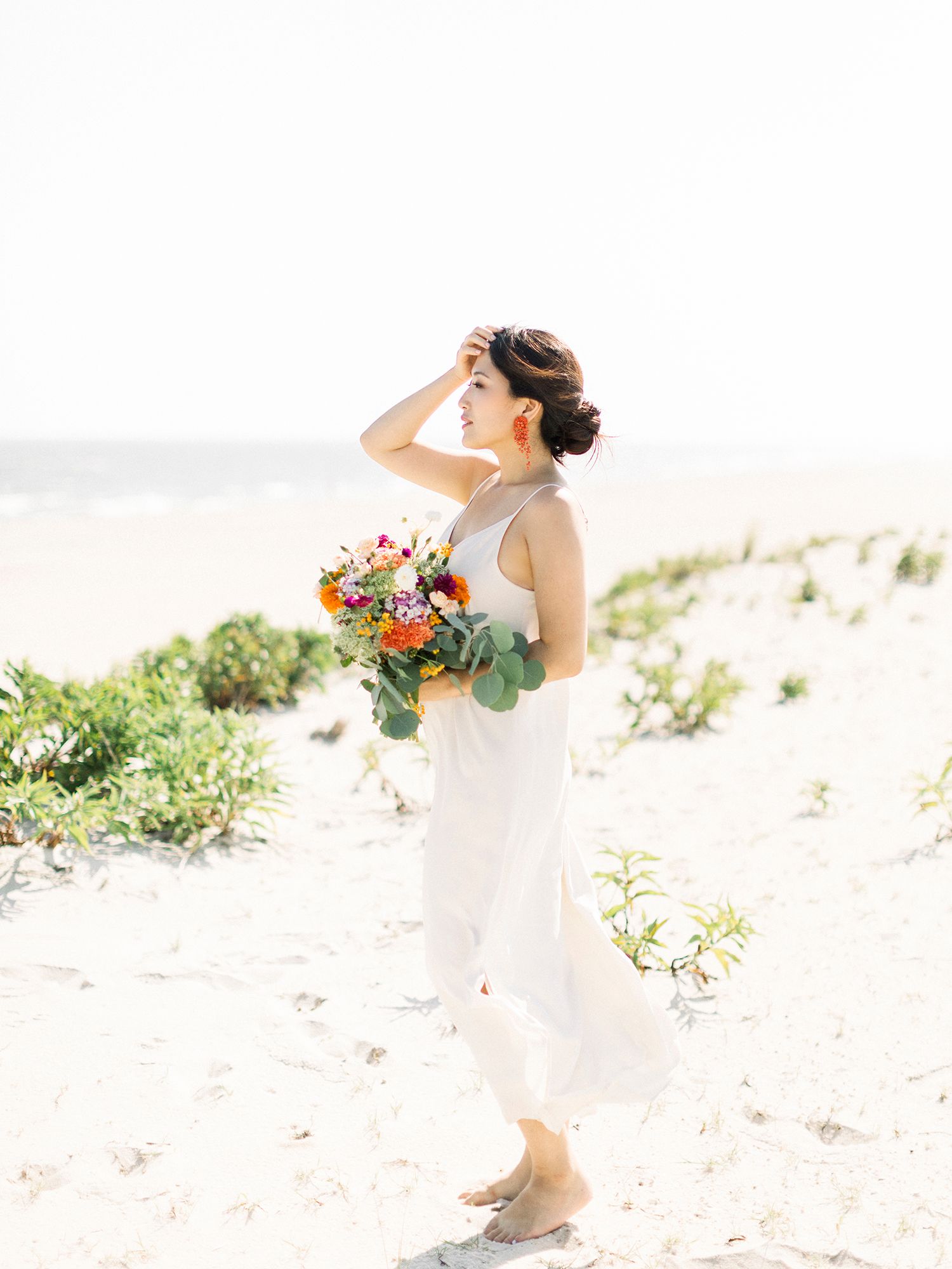 Figure in flowing white dress twirling on a sandy beach with flowers.