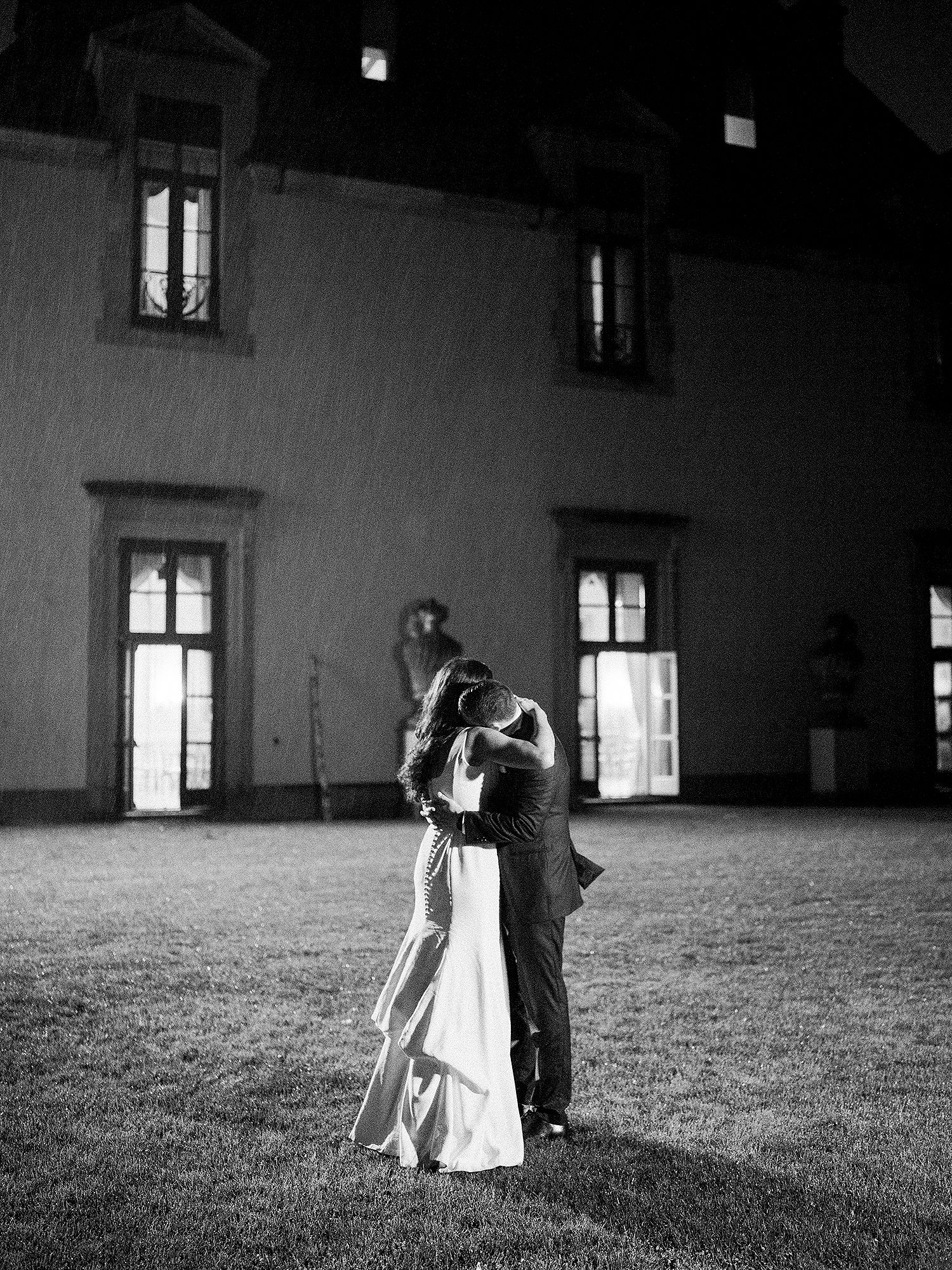 A couple in formal wedding attire dance in a dramatic black and white indoor space with large windows. NYC wedding photographer.