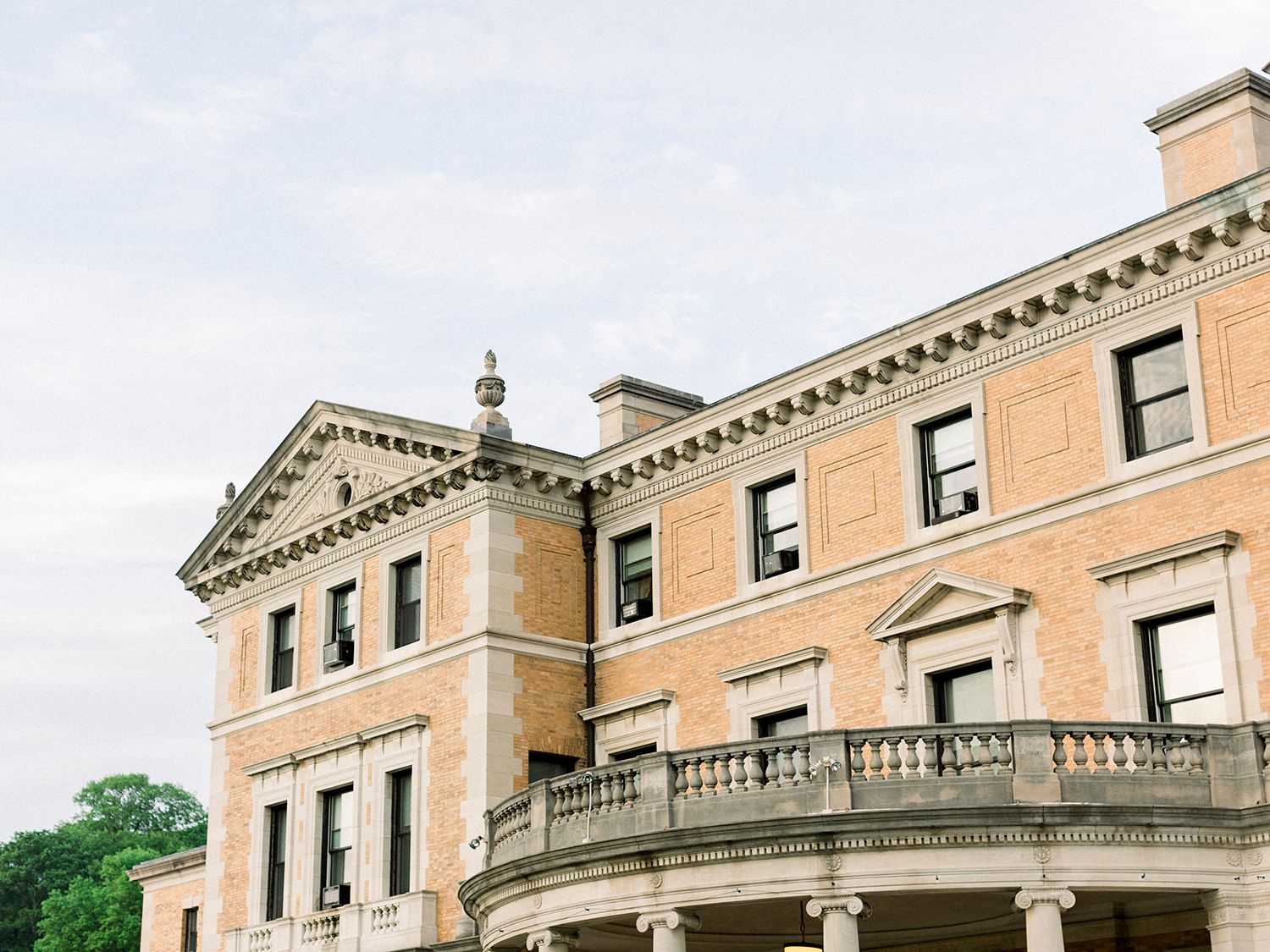 Historic mansion with neoclassical architecture and ornate stone balcony against blue sky.