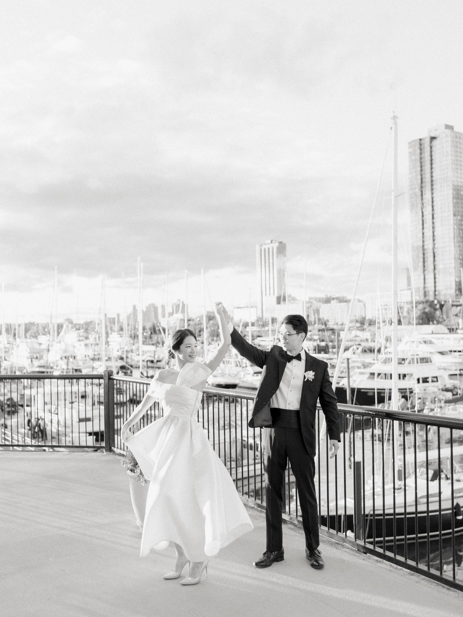 Newlyweds dance playfully on a rooftop terrace with urban skyline views.