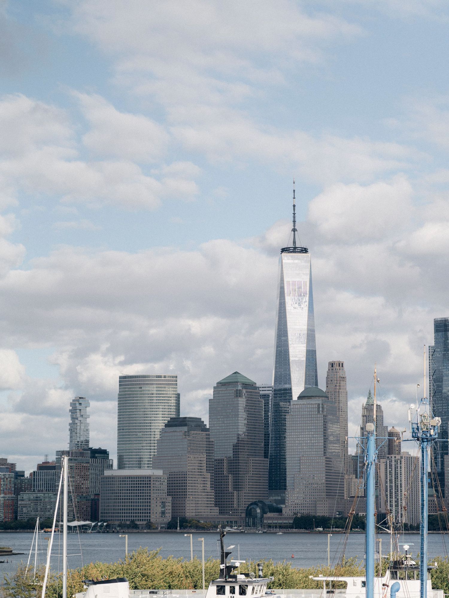 Panoramic view of New York City skyline with boats and marina in foreground under cloudy sky.