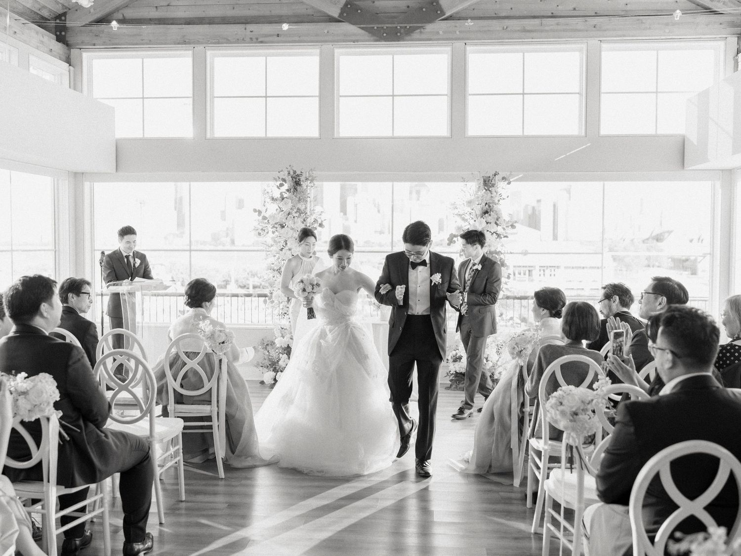 Wedding venue interior with elegant white chairs and natural lighting through large windows.