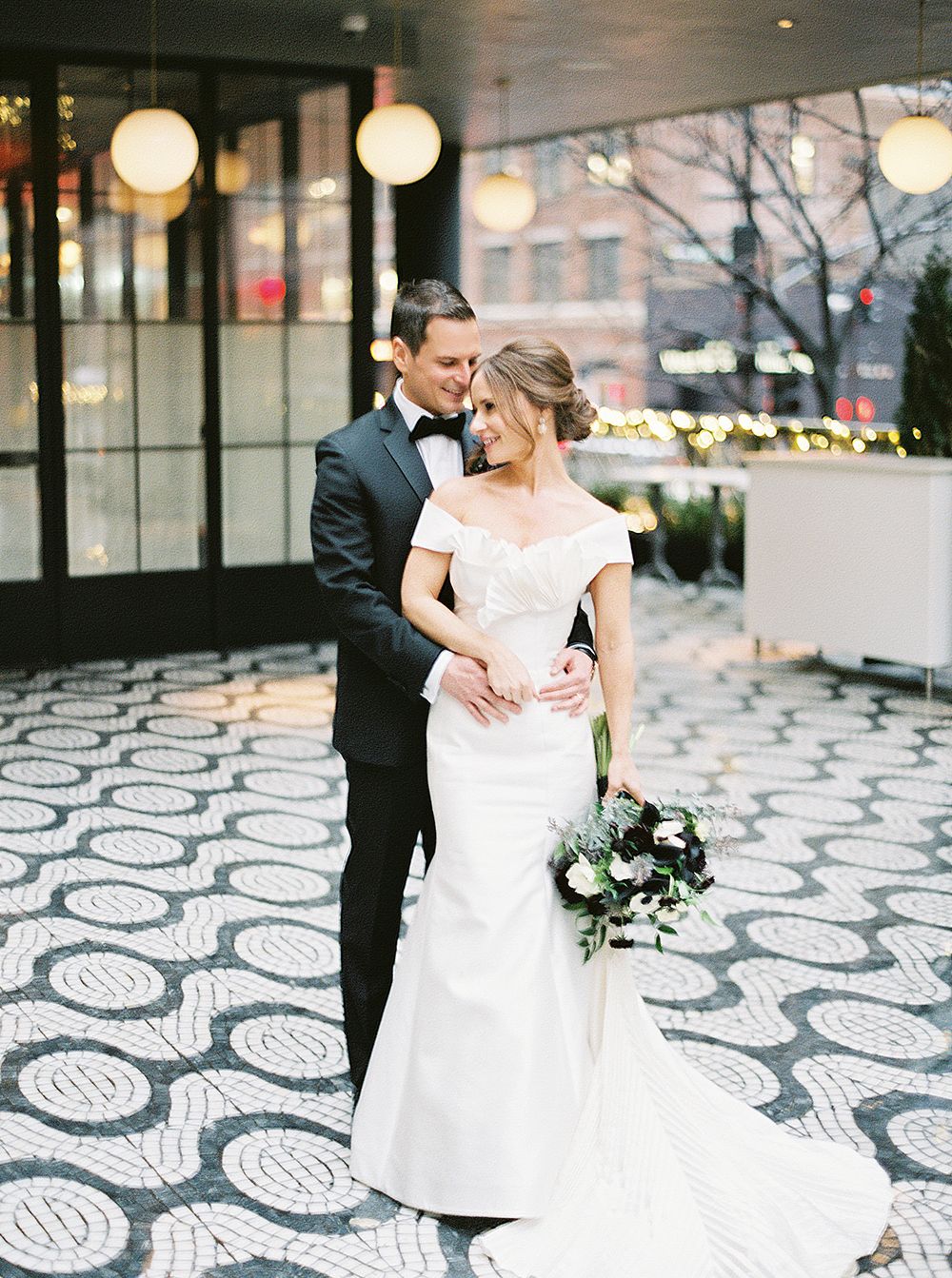 A romantic wedding photo of a couple embracing on a geometric patterned floor with hanging globe lights. NYC wedding photographer.