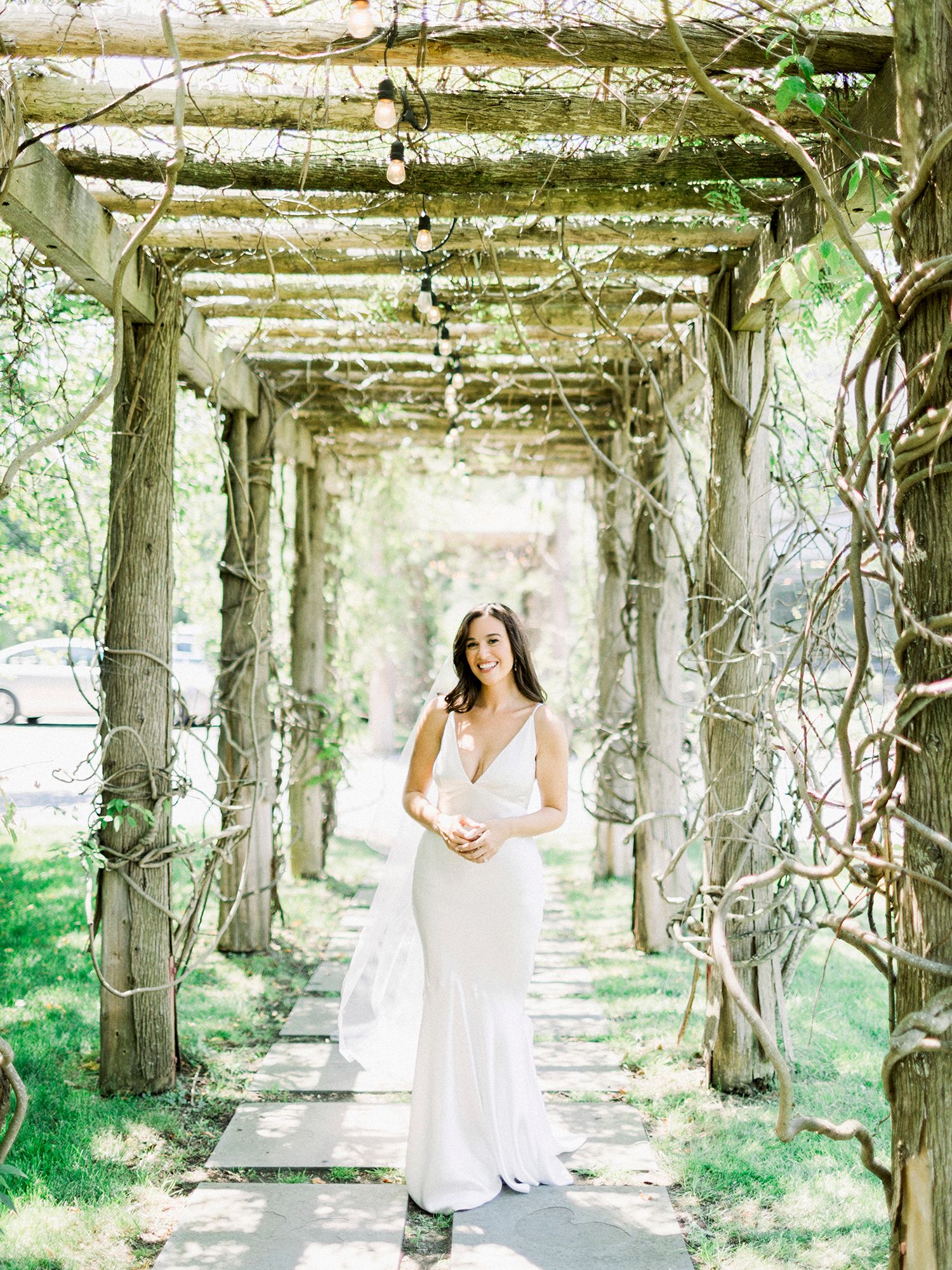 Woman in white dress standing beneath a vine-covered garden archway.