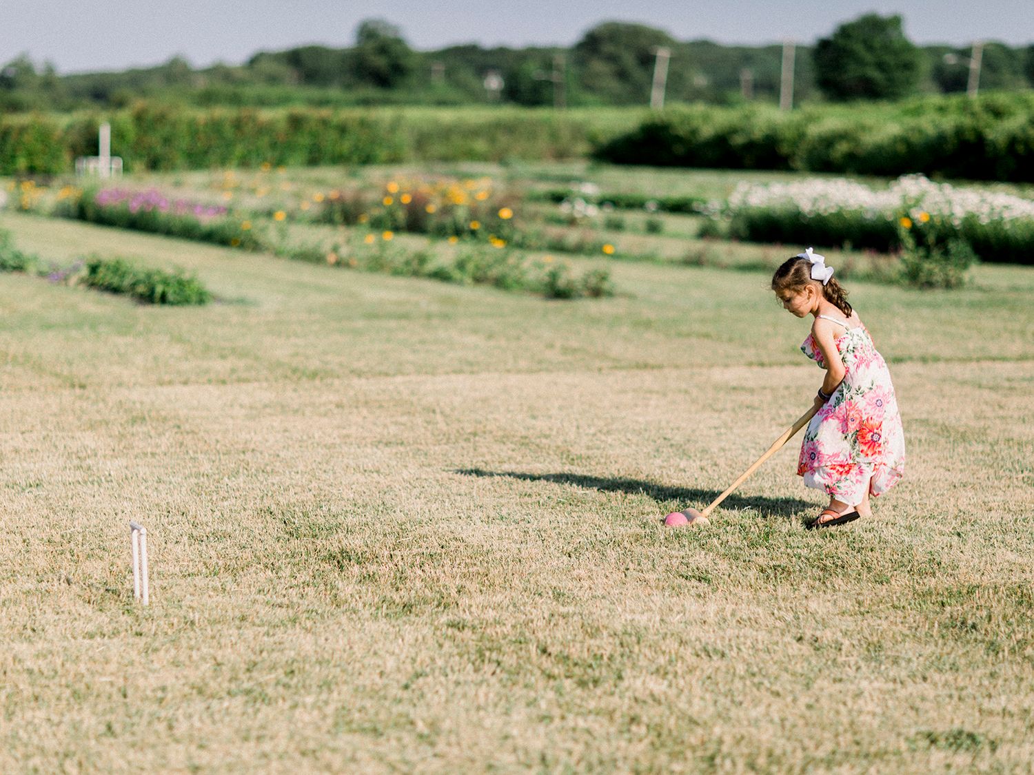 Young guest in pink dress plays croquet on lawn during wedding reception.