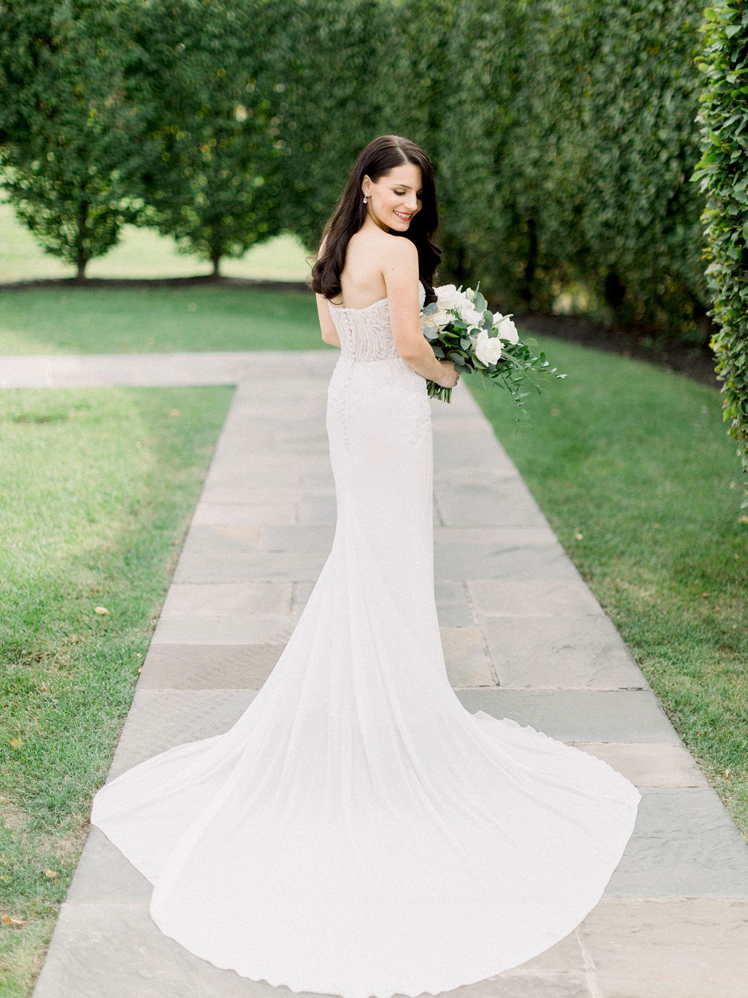 Flowing white wedding dress captured in movement along garden pathway.