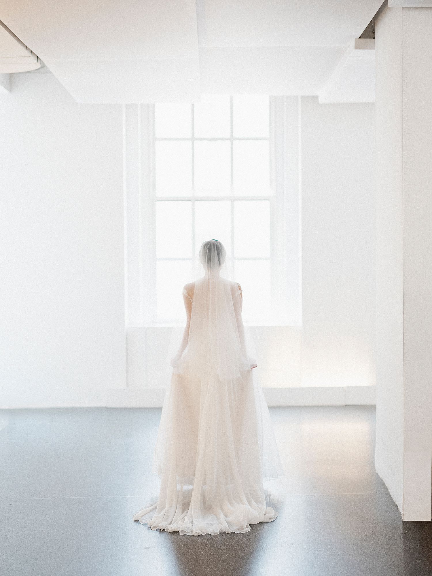 An ethereal white wedding dress hangs in a bright, minimalist room with natural light. NYC wedding photographer.