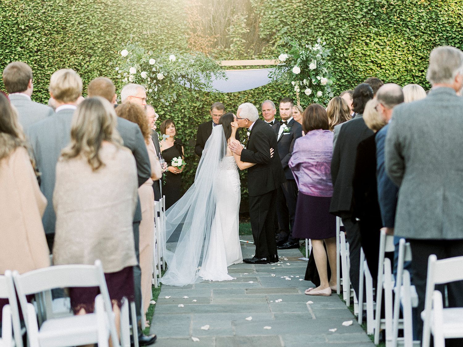 Wedding guests seated in white chairs for outdoor garden ceremony.