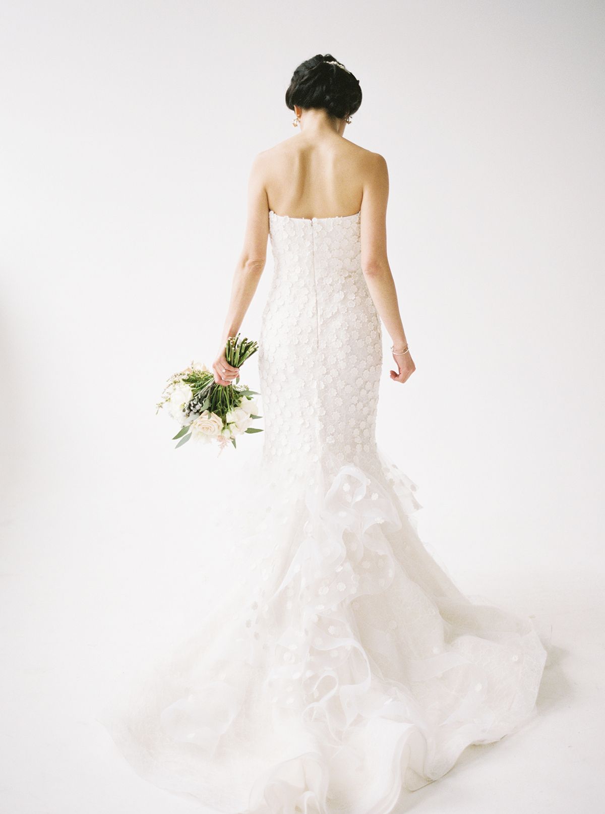Bride in flowing lace gown twirls against white backdrop.