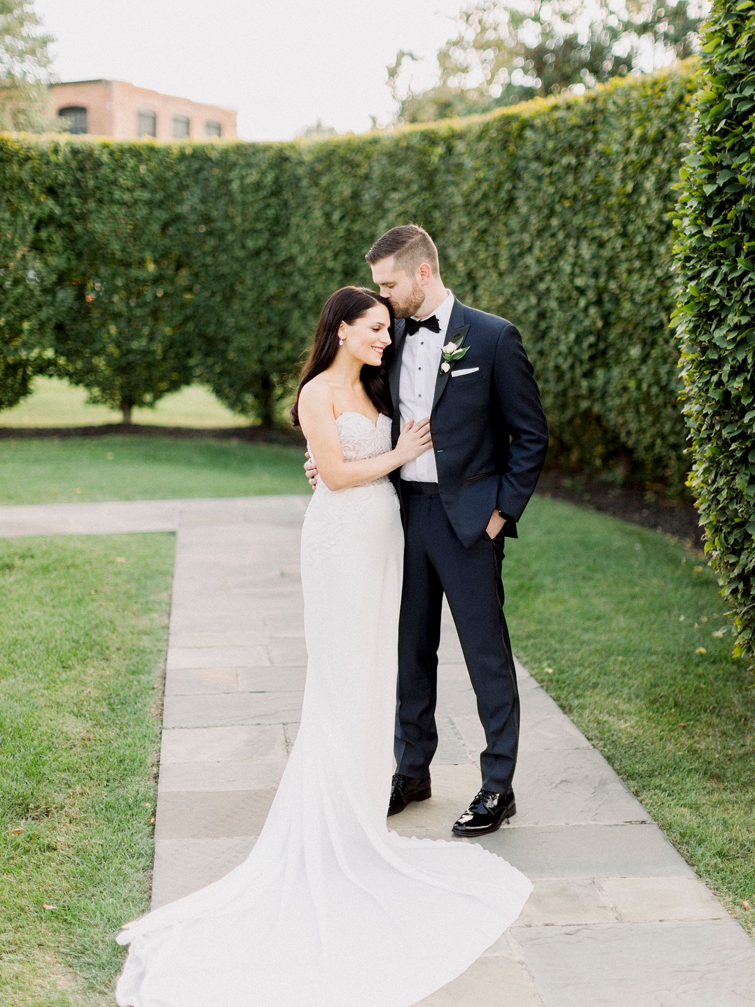 Wedding couple walking along a garden path bordered by manicured hedges. NYC wedding photographer.