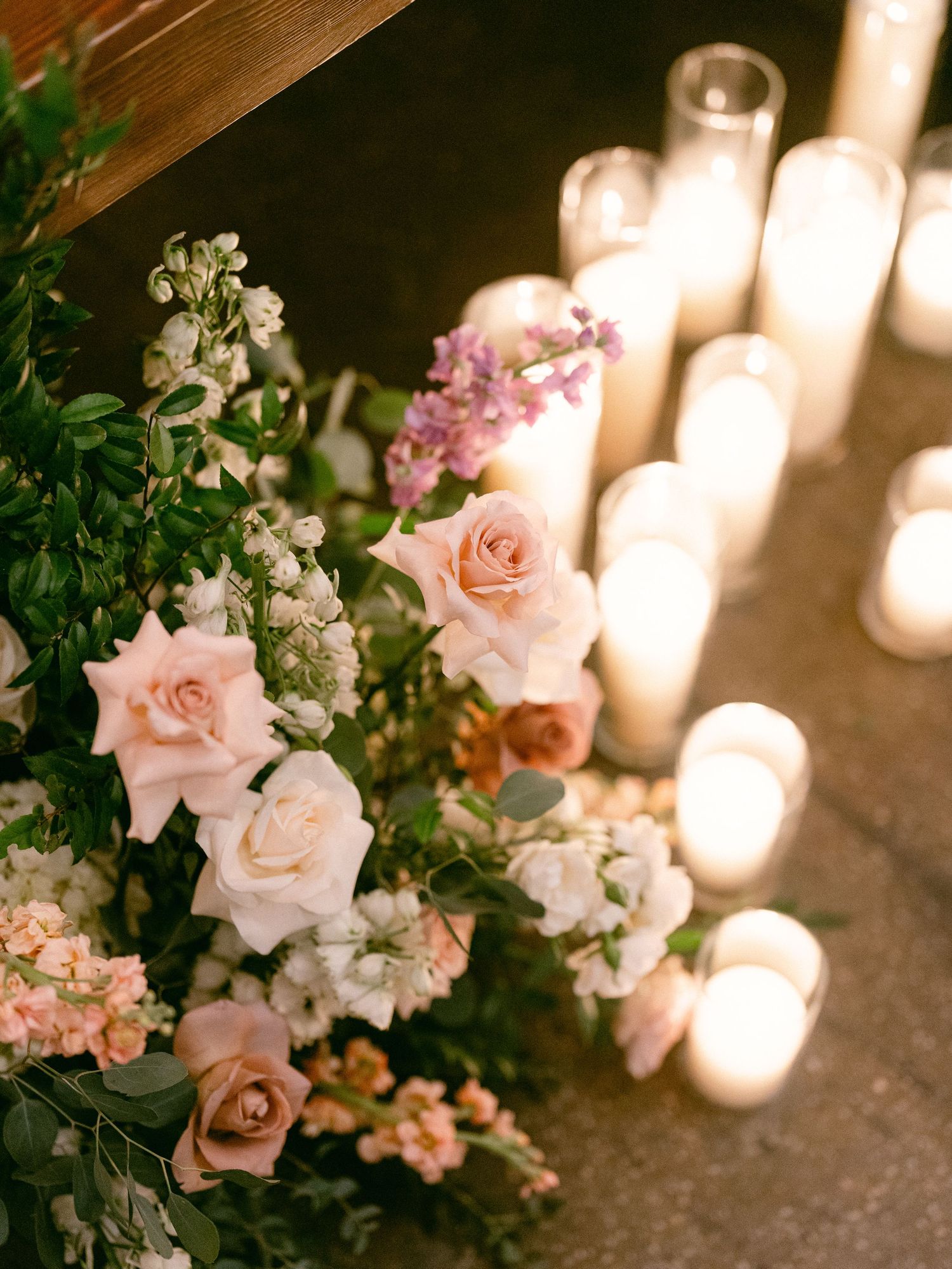Soft pink roses and white flowers arranged beside glowing pillar candles creating a romantic ambiance.