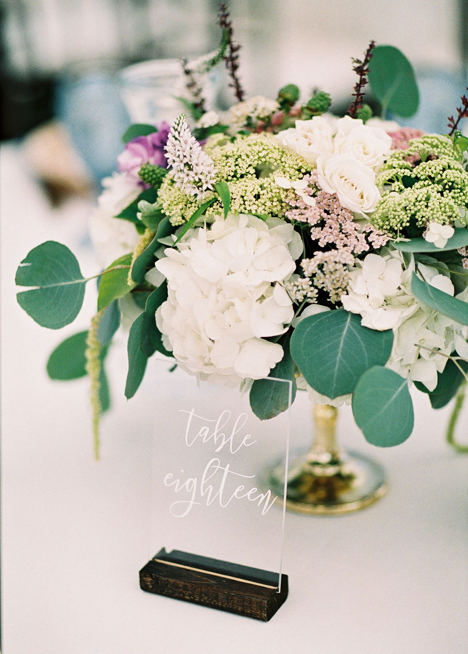 Elegant table numbers with white floral centerpieces and eucalyptus leaves on wedding reception tables.