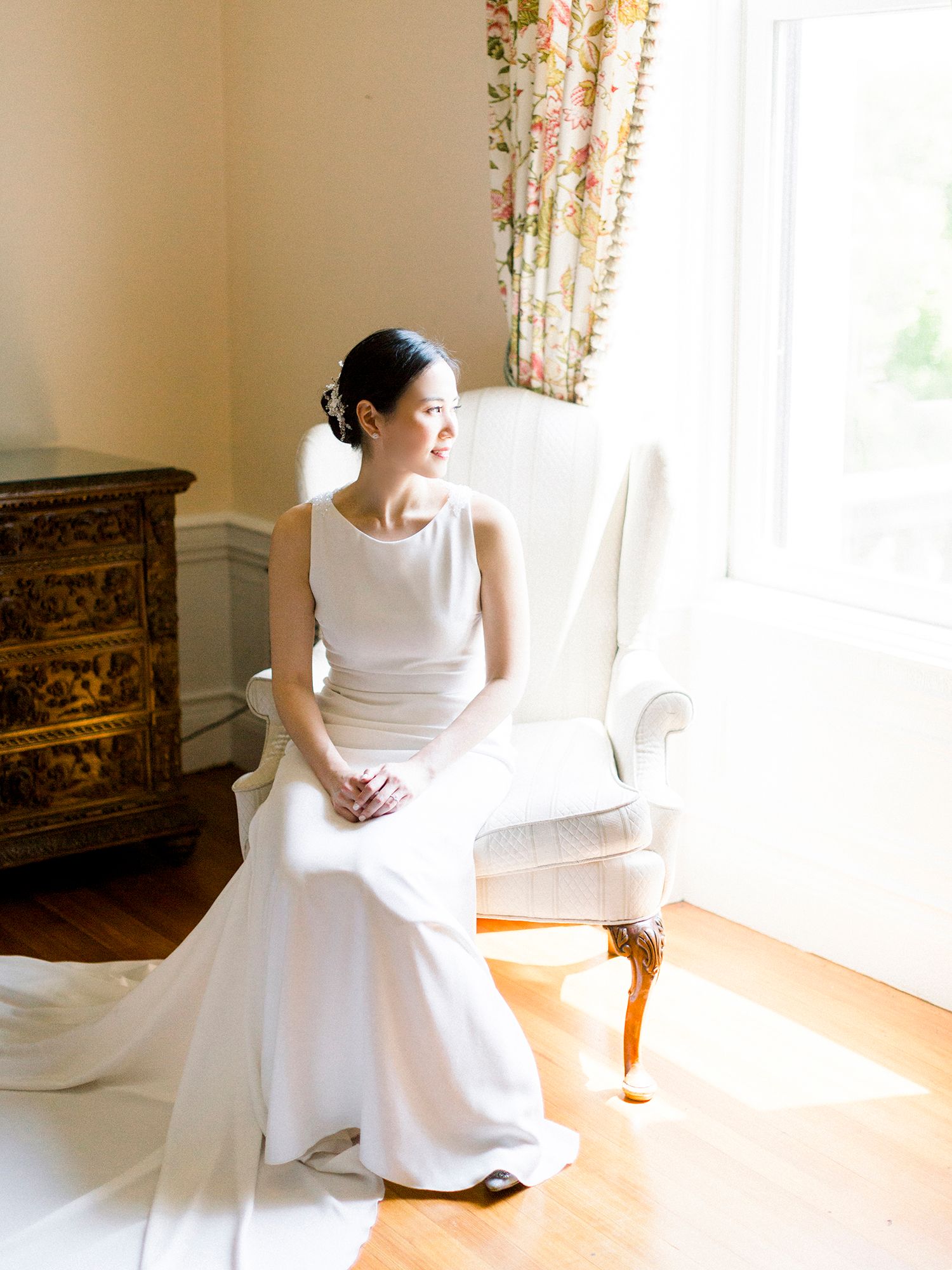 Sunlit bridal portrait in a classic white gown against vintage interior decor.