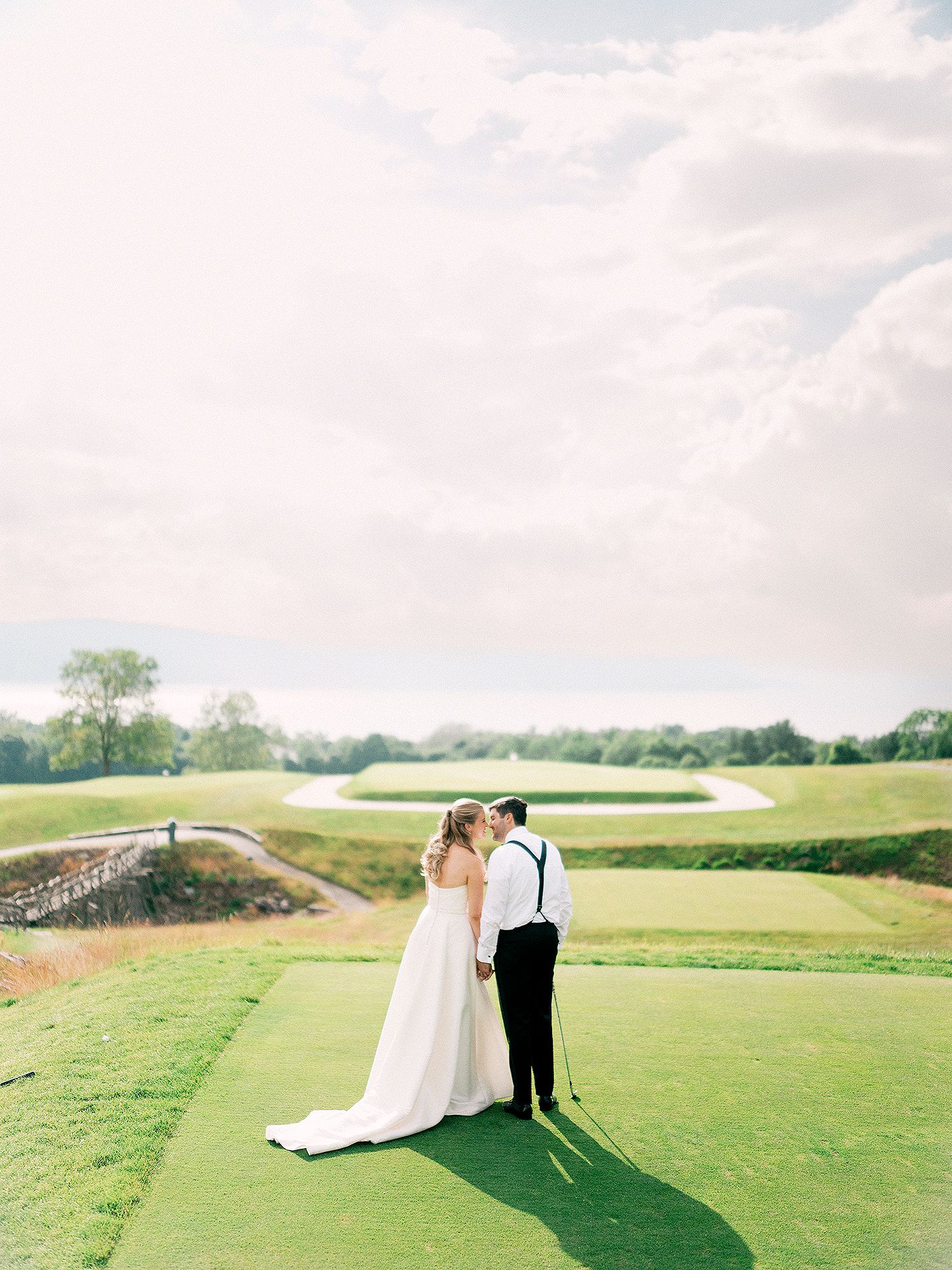 A wedding couple shares an intimate moment on a scenic golf course with rolling hills in the background. NYC wedding photographer.