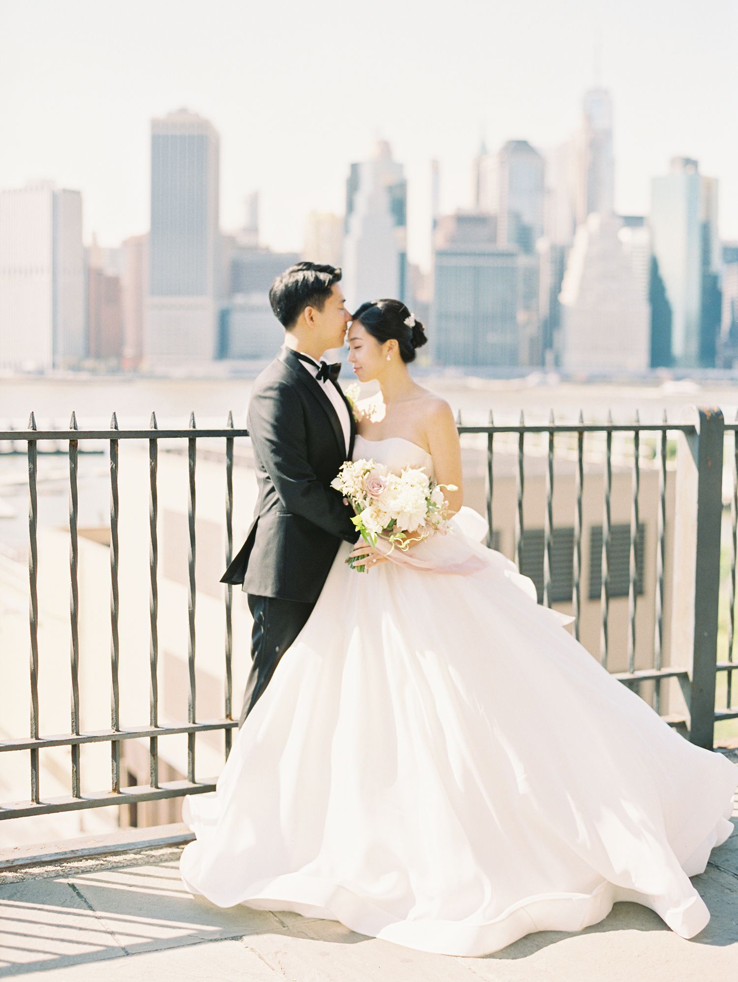 Wedding couple poses against city skyline backdrop with flowing white dress. NYC wedding photographer.