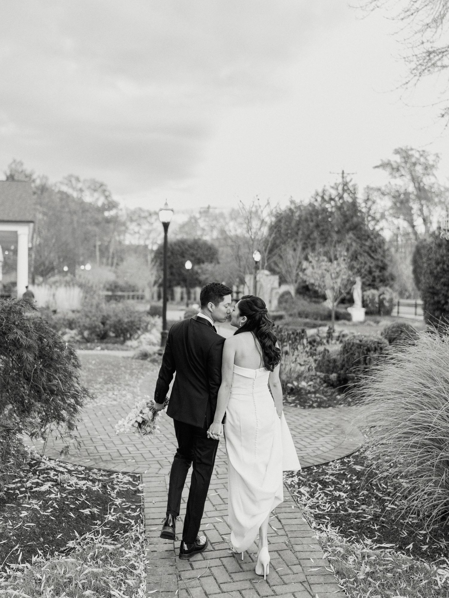 Black and white wedding photos of a couple walking along a garden pathway.