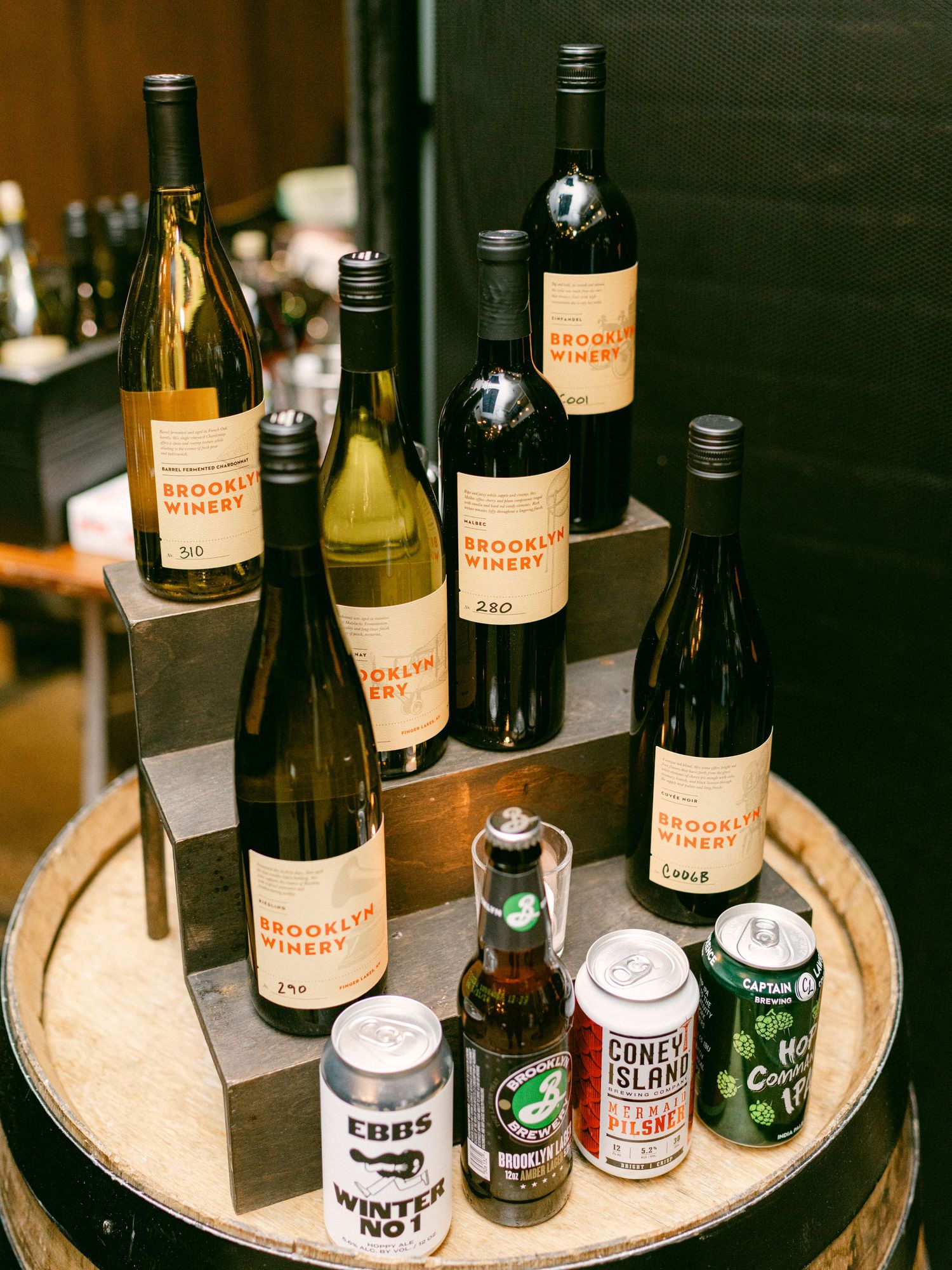 Collection of wine bottles and craft beer cans arranged on a wooden circular tray.