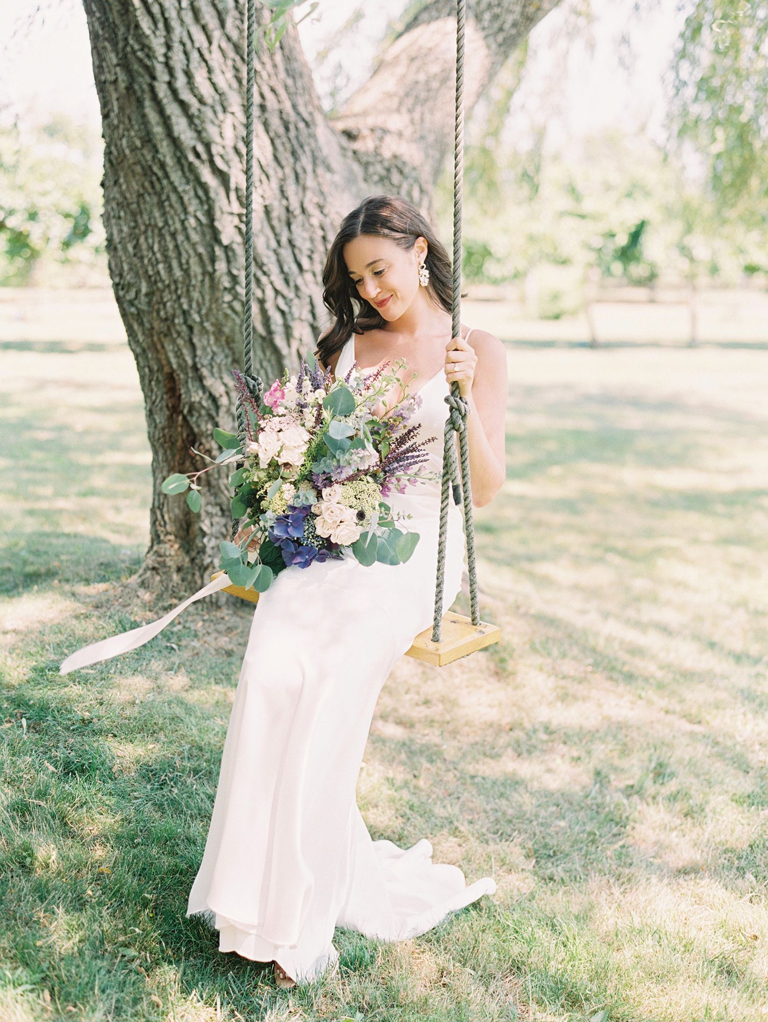 Beautiful bridal portrait series with flowing white dress and romantic floral bouquet against a rustic tree backdrop. NYC wedding photograph