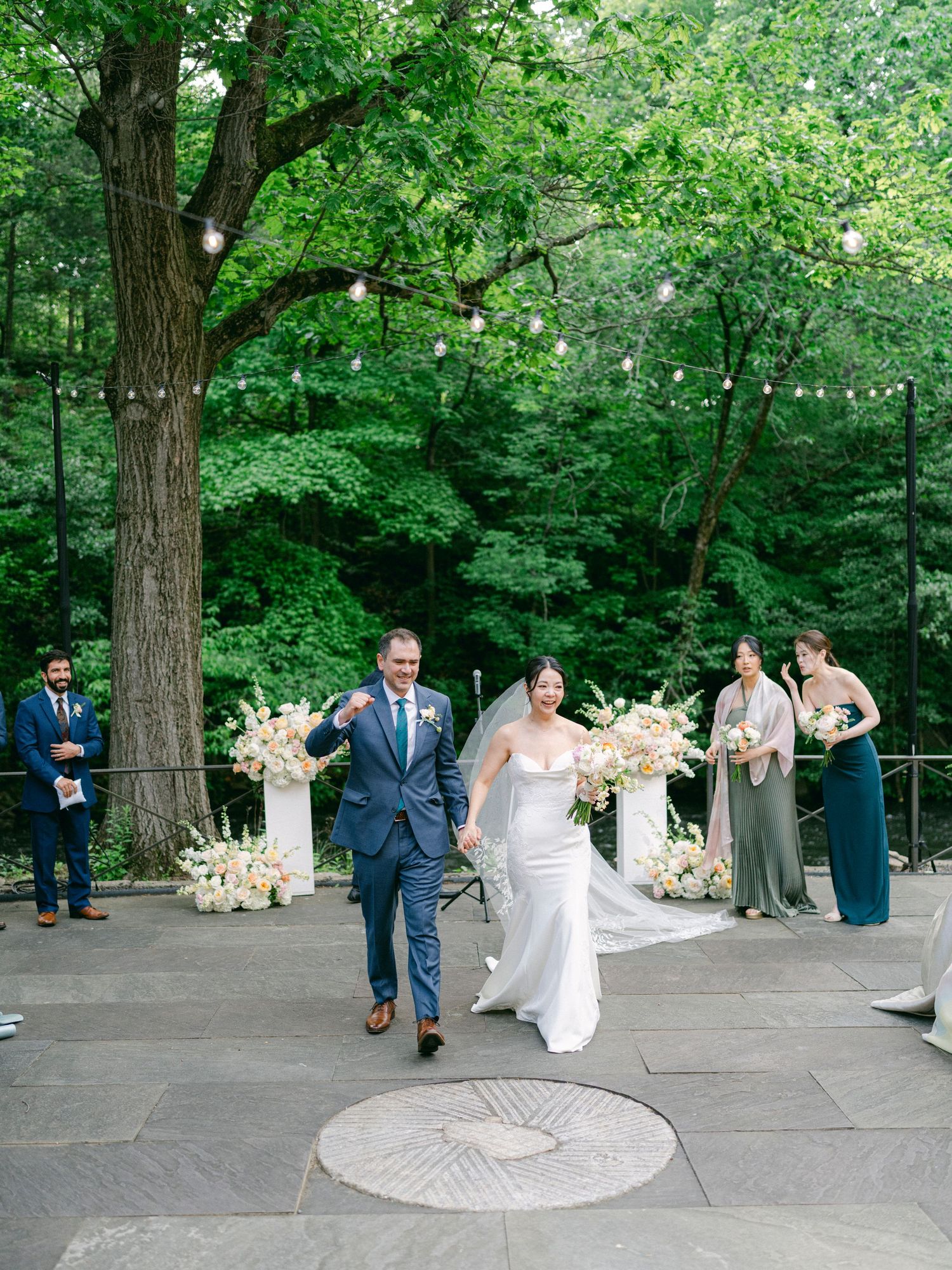 A wedding ceremony setup with string lights and floral arrangements in a wooded outdoor setting.