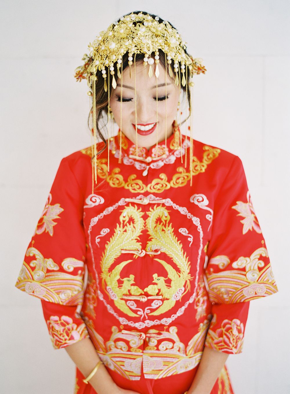 Traditional Chinese bride wearing an ornate red qipao with gold phoenix crown and decorative details. NYC wedding photographer.