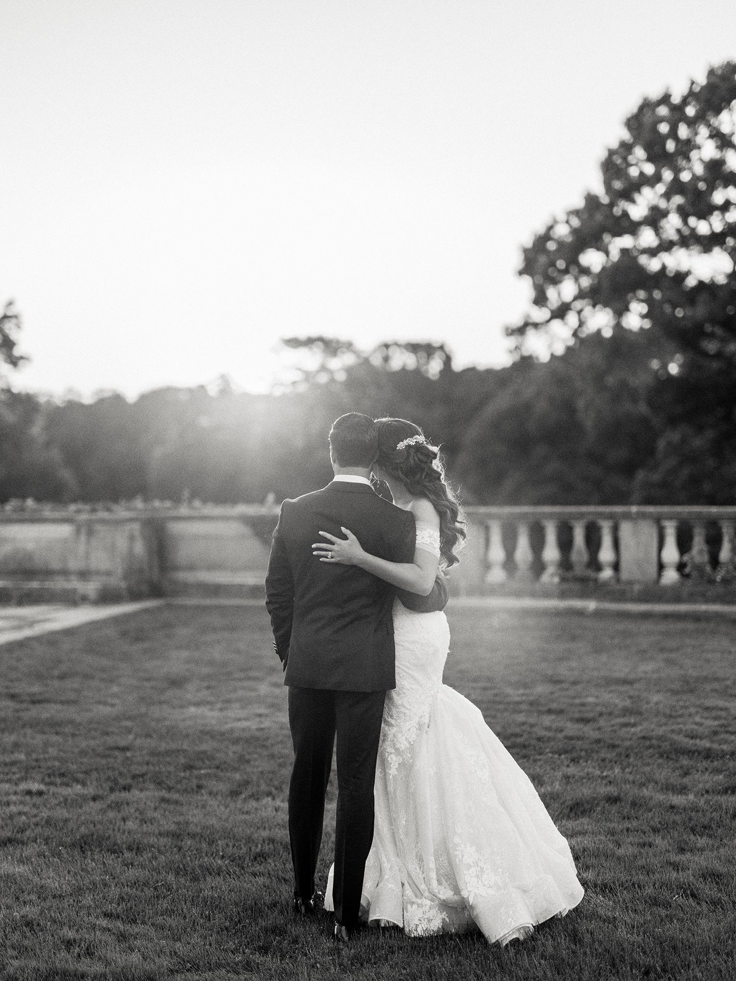 Black and white portrait of a couple embracing on manicured grounds at sunset. NYC wedding photographer.