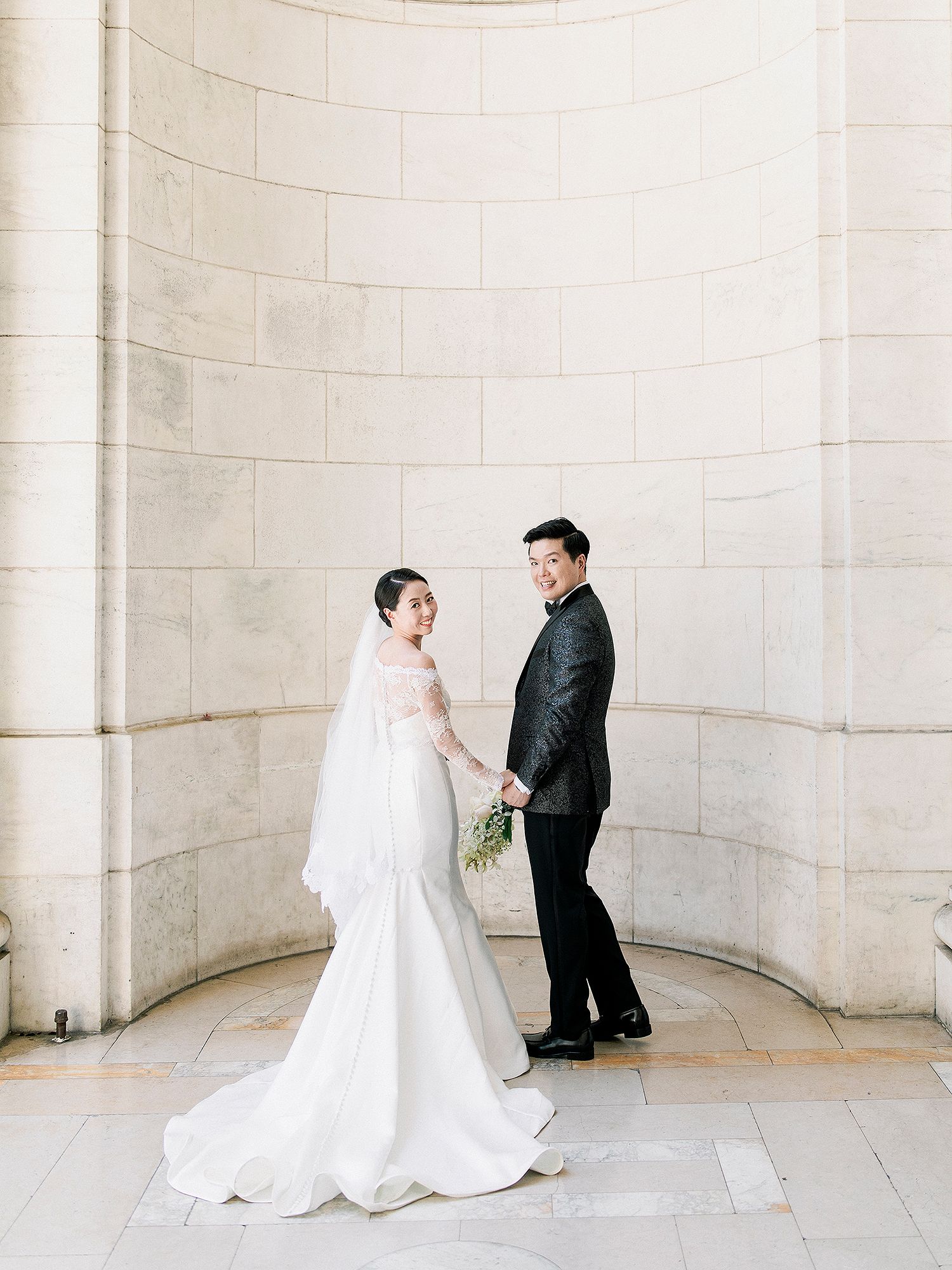 A couple in wedding attire dances and twirls in an elegant white stone colonnade. NYC wedding photographer.