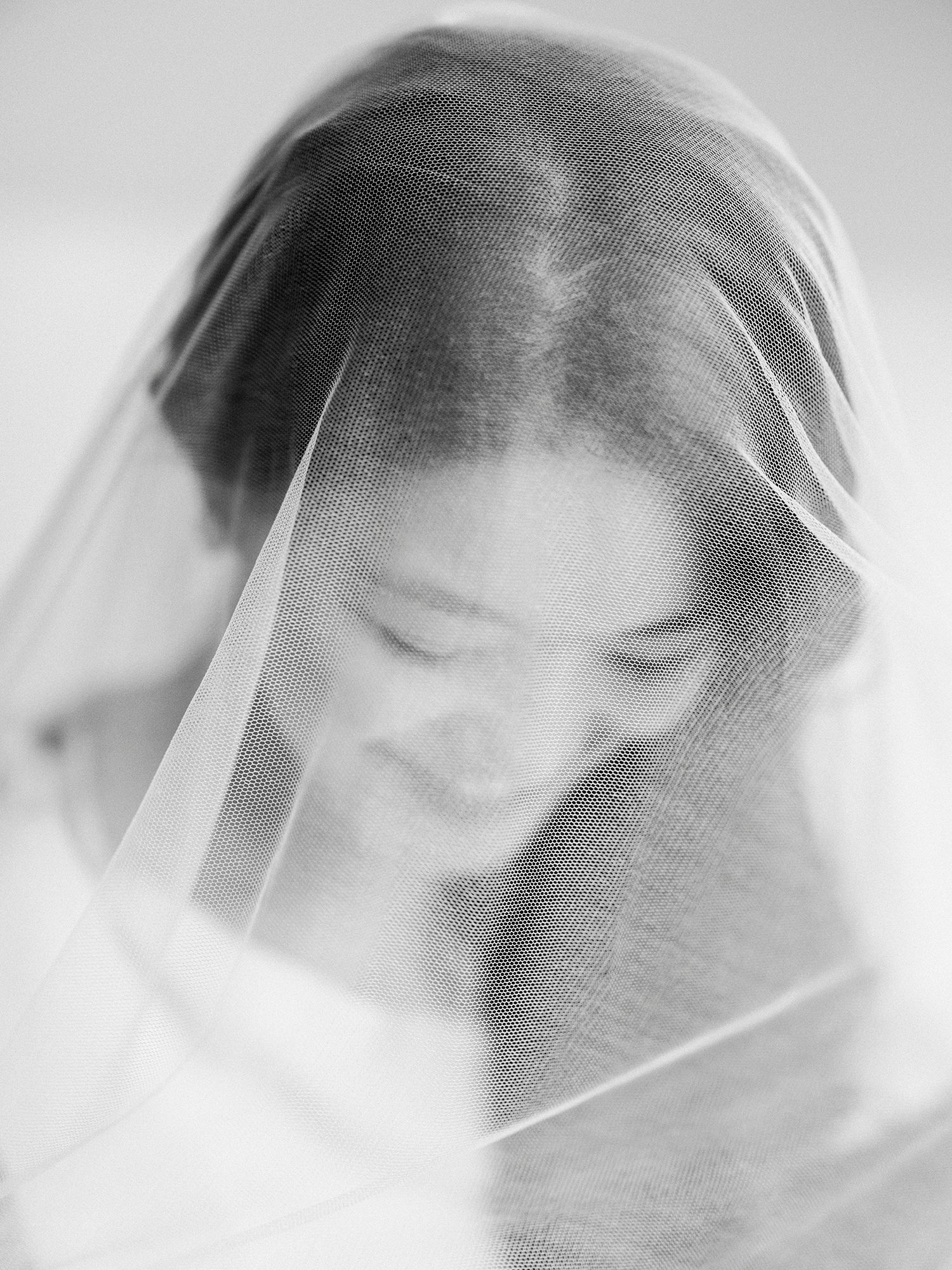 Dreamy black and white portrait through a sheer wedding veil creating an artistic blur effect.