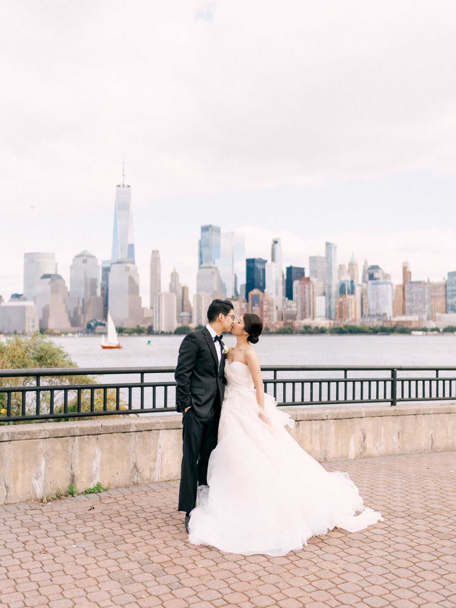Wedding couple posing along waterfront with Manhattan skyline view in background.