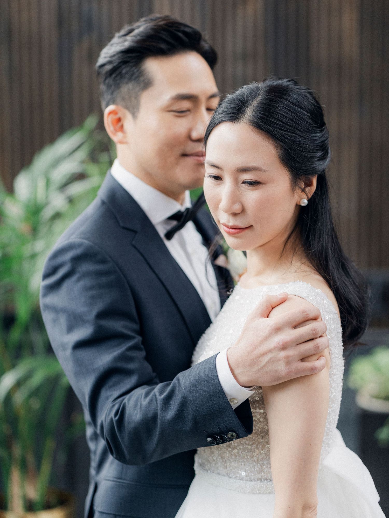 Intimate wedding portrait against wooden wall backdrop with natural lighting.