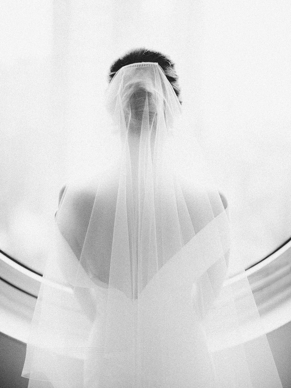 Ethereal black and white photo of a bride wearing a flowing veil from behind.