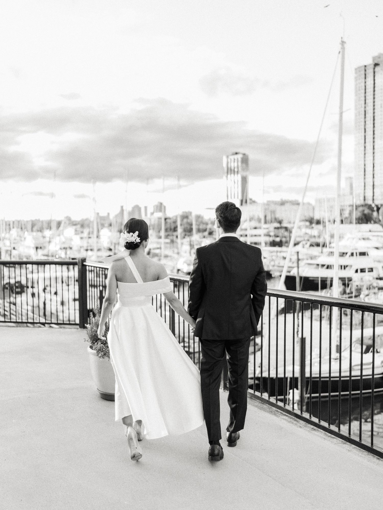 Black and white photo of a couple walking along a marina boardwalk.