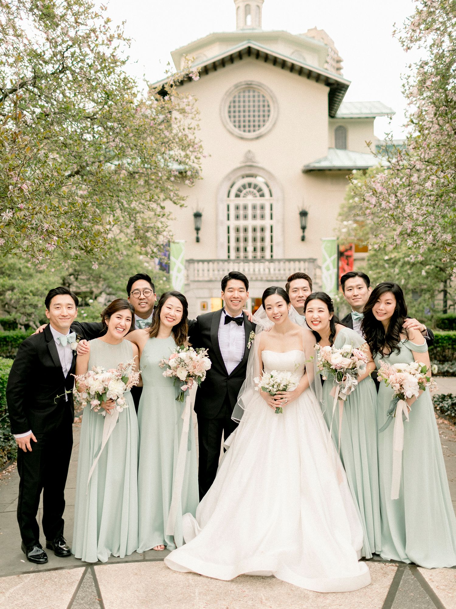 Wedding party poses in front of church with bridesmaids wearing soft mint green dresses. NYC wedding photographer.