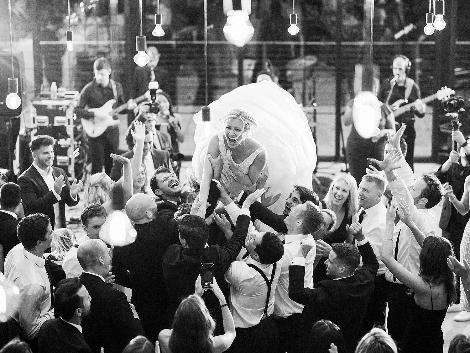 Wedding reception dance party with hanging lights and a crowd of celebrating guests. NYC wedding photographer.