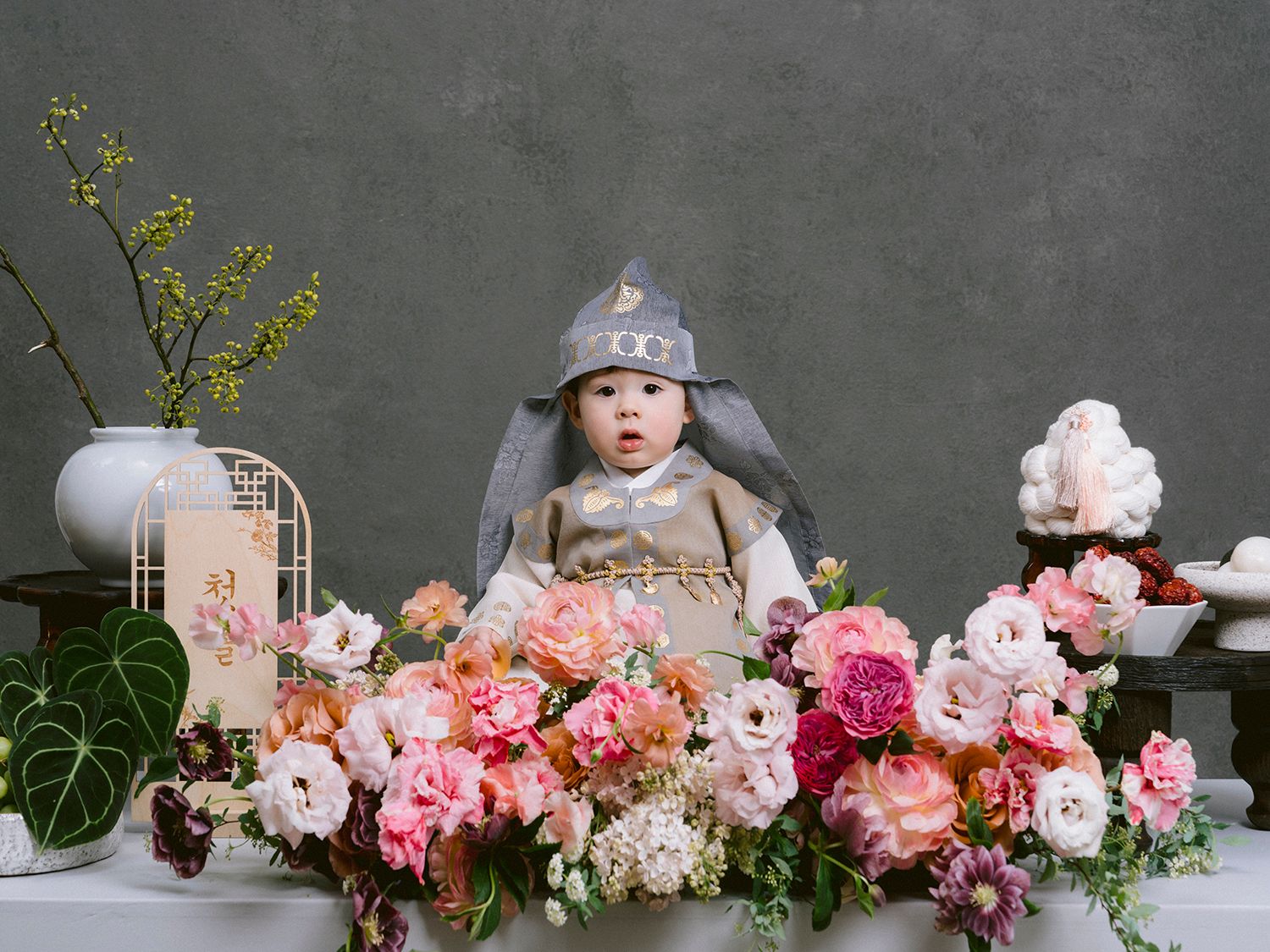 Panoramic sequence showing pink and white peonies arranged with greenery against a dark gray concrete wall.
