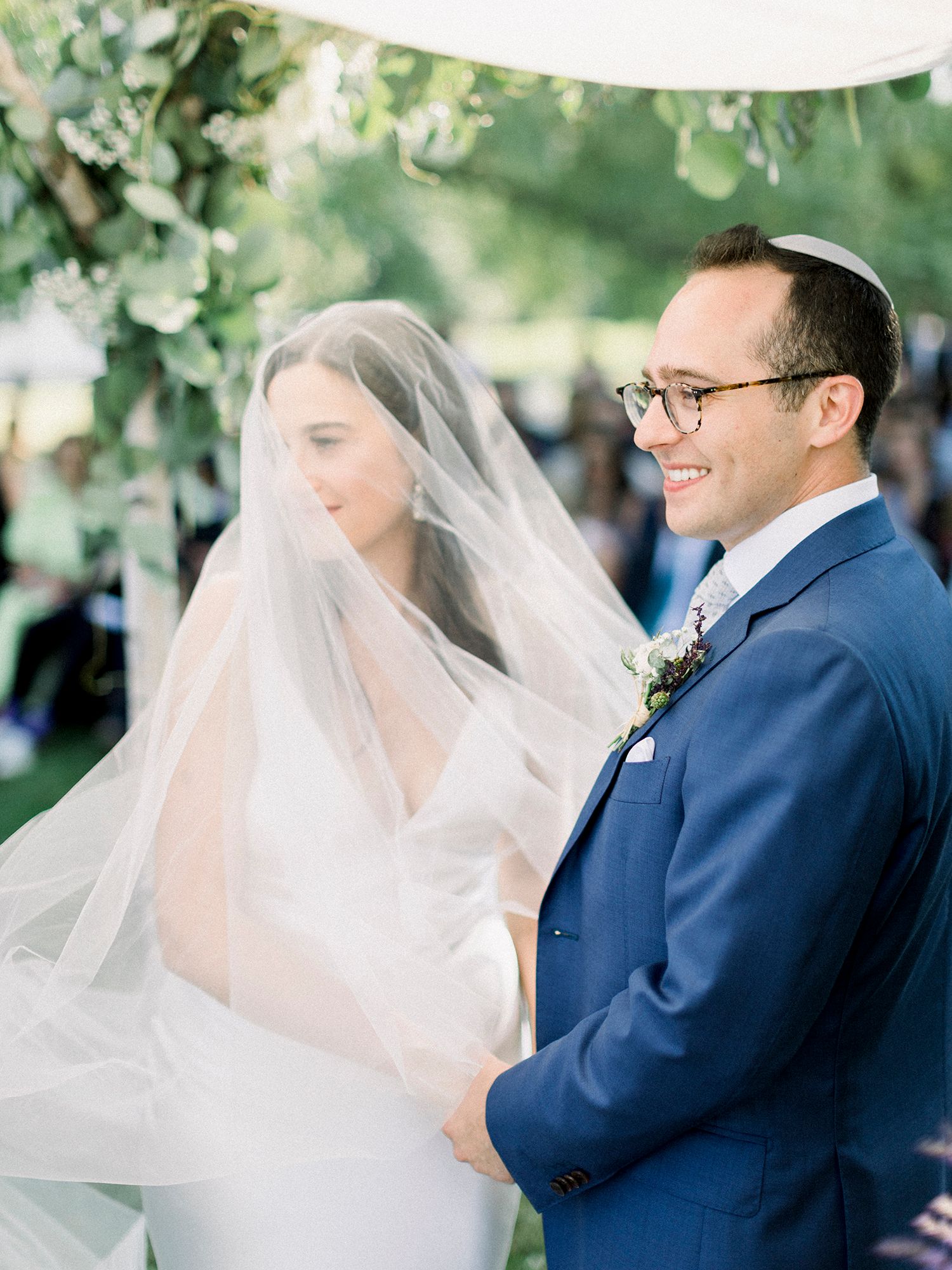 Joyful couple shares a moment during their outdoor wedding ceremony under green trees.